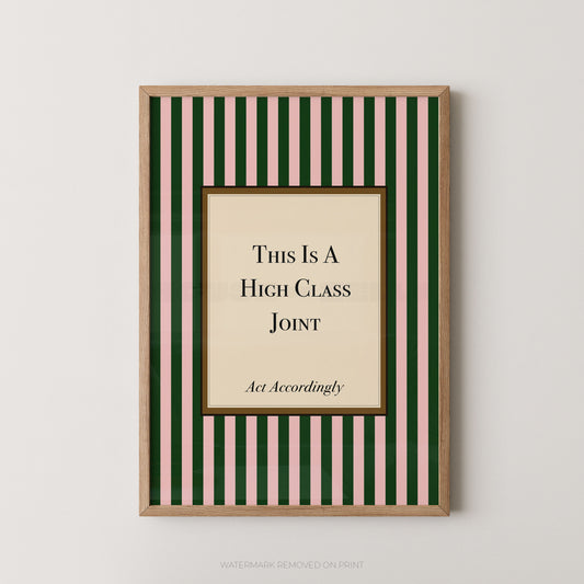 A framed humorous wall art print featuring a beige central panel with the text 'This Is A High Class Joint' and 'Act Accordingly' on a background of dark green and light pink vertical stripes, enclosed in a light wood frame.