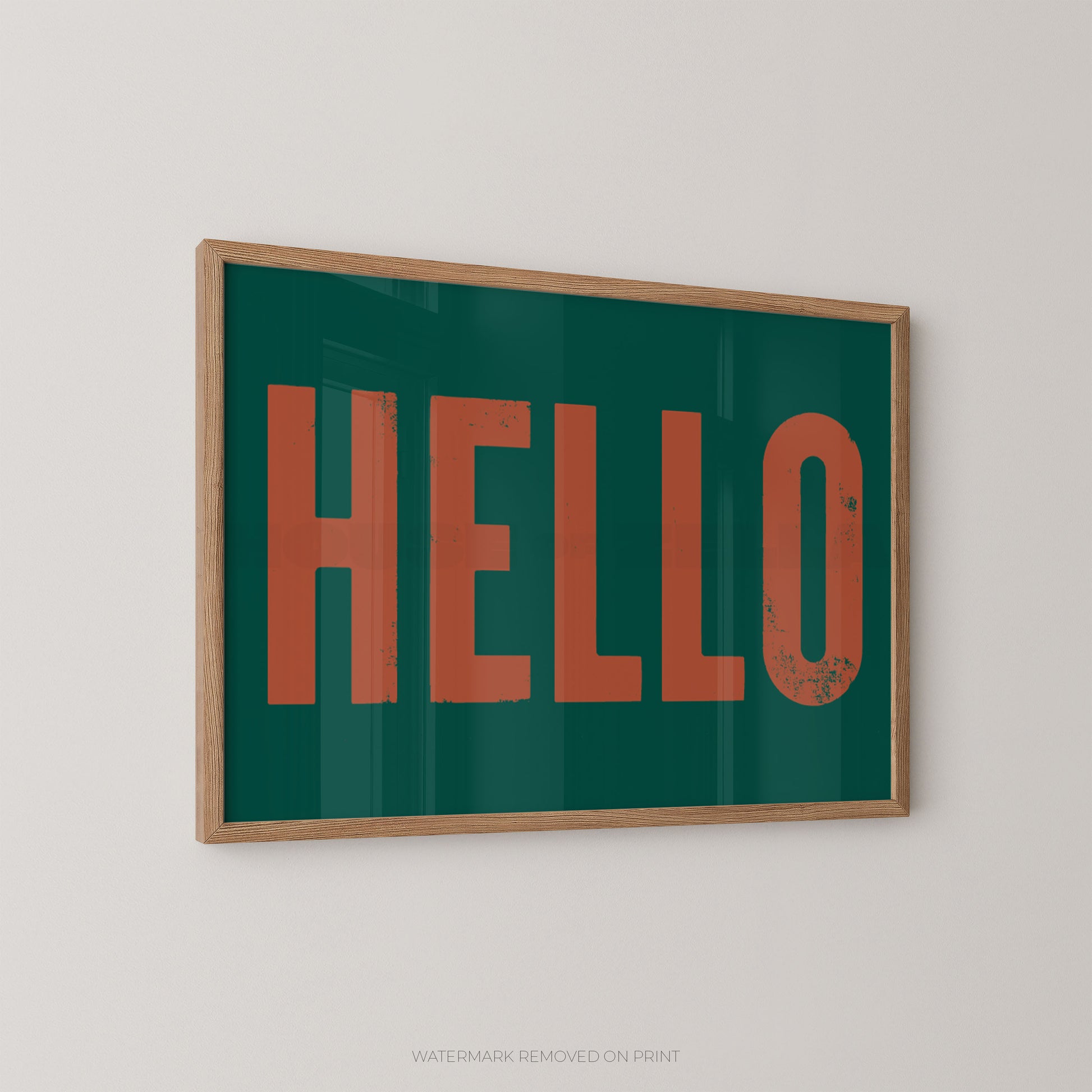 Framed wall art print with the word "HELLO" in large rust-orange letters on a dark teal-green background, shown hanging on a light gray wall.