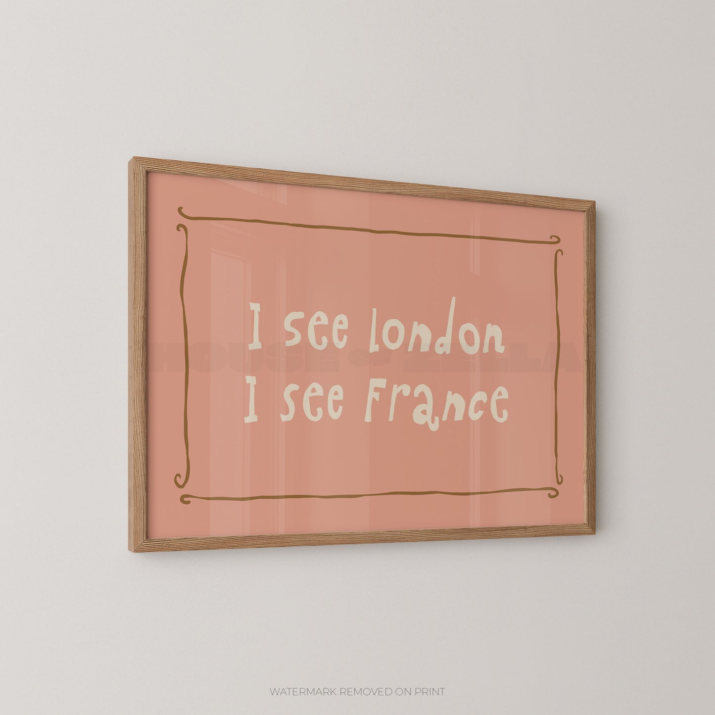 A framed typographic wall art print hanging on a light gray wall. The print has a dusty pink background with white handwritten-style text reading 'I see London I see France' and a thin brown decorative border.