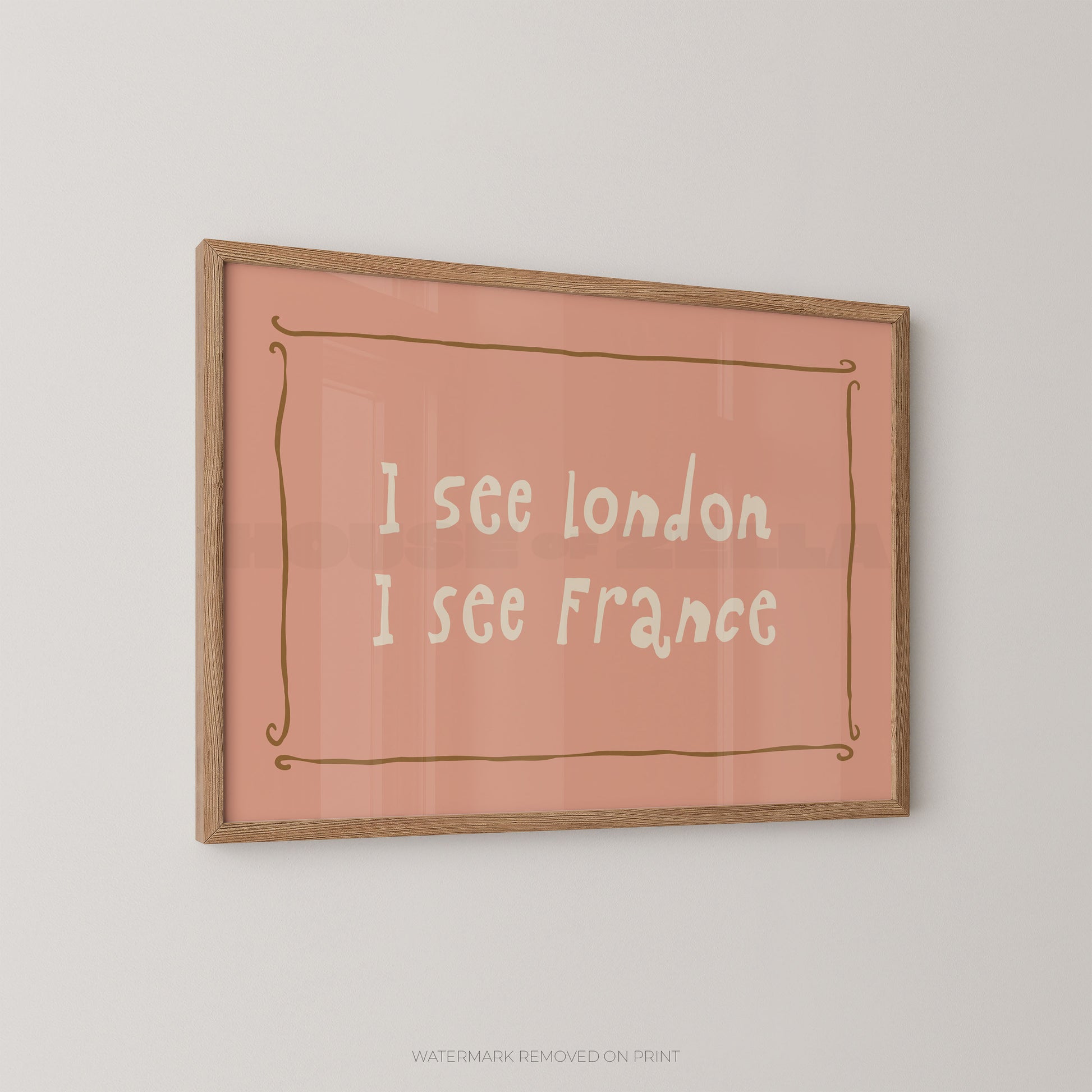 A framed typographic wall art print hanging on a light gray wall. The print has a dusty pink background with white handwritten-style text reading 'I see London I see France' and a thin brown decorative border.