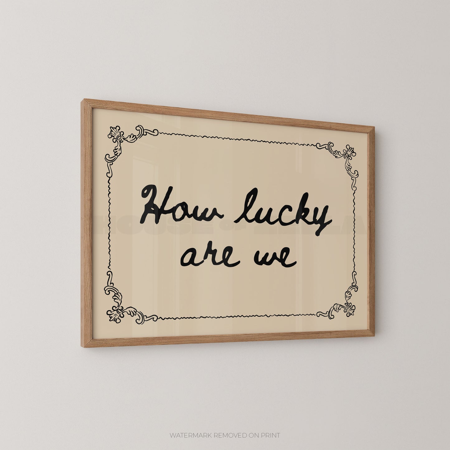 Framed wall art with the phrase “How lucky are we” in black script inside a light wood frame, shown hanging on a plain light gray wall.