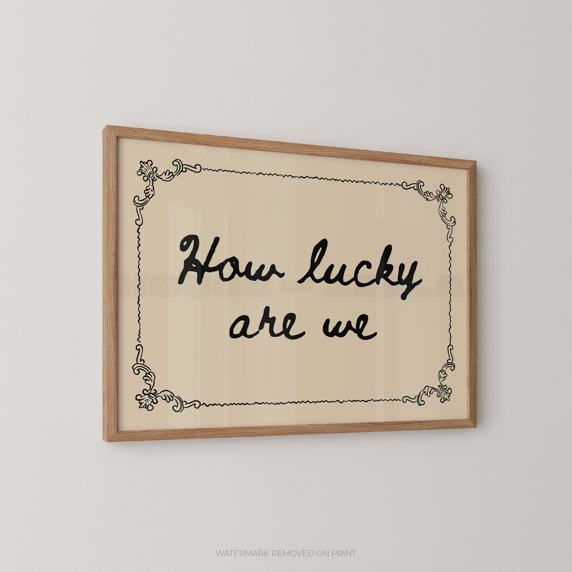 Framed wall art with the phrase “How lucky are we” in black script inside a light wood frame, shown hanging on a plain light gray wall.
