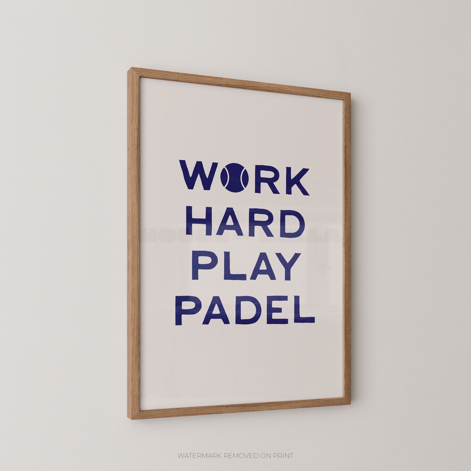 A framed typographic wall print with the phrase “WORK HARD PLAY PADEL” in dark blue text on a white background, shown hanging on a light neutral wall. The print has a light natural wood frame and a small tennis ball icon replacing the letter O in “WORK.