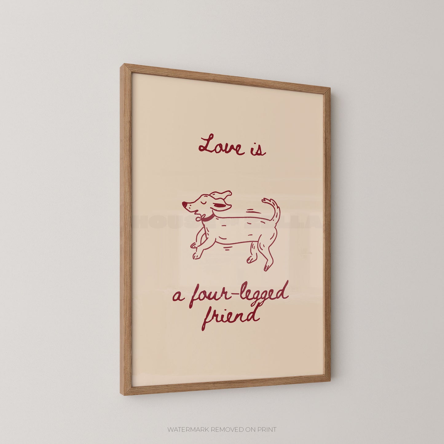 A framed art print featuring a minimalist red line drawing of a dog with the text 'Love is a four-legged friend' on a cream background, enclosed in a light wood frame and shown hanging on a light gray wall.
