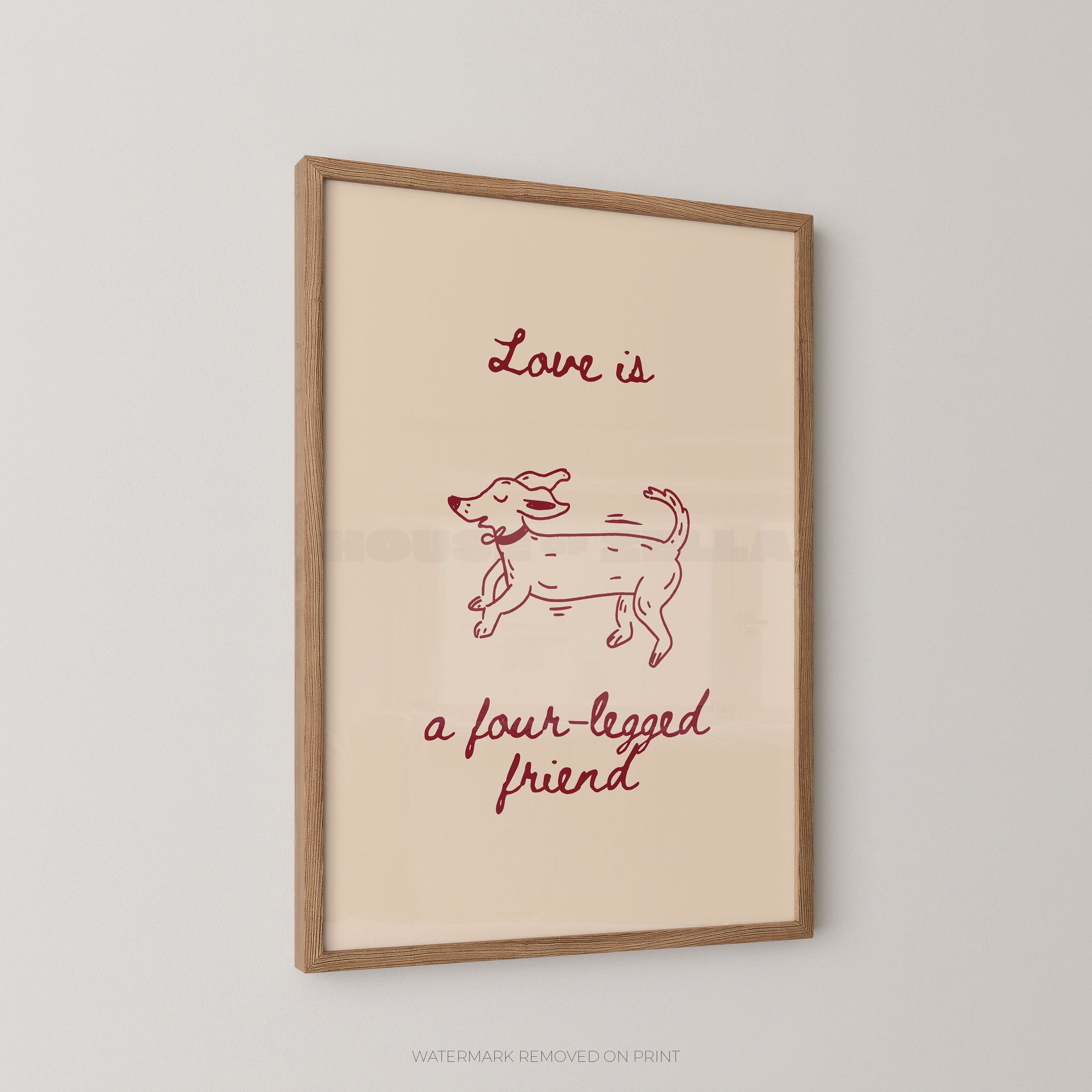 A framed art print featuring a minimalist red line drawing of a dog with the text 'Love is a four-legged friend' on a cream background, enclosed in a light wood frame and shown hanging on a light gray wall.