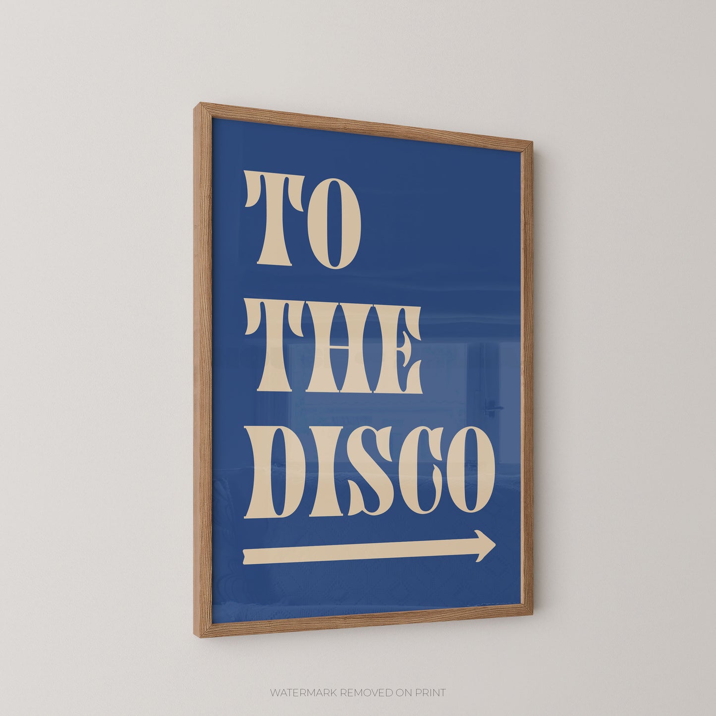 Framed wall art print with the words “TO THE DISCO” in large cream lettering on a blue background, with a cream arrow beneath. The print is shown hanging on a light neutral wall.