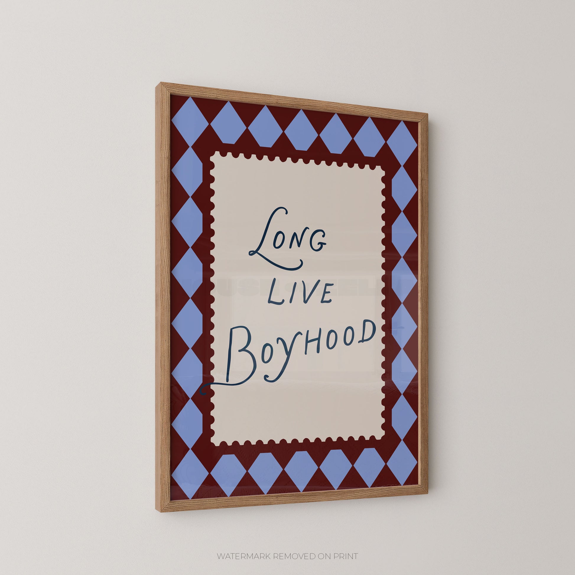Framed wall art featuring the phrase 'Long Live Boyhood' in dark blue script on an off-white center panel, surrounded by a blue and burgundy diamond border and a light wood frame, shown hanging on a light gray wall.