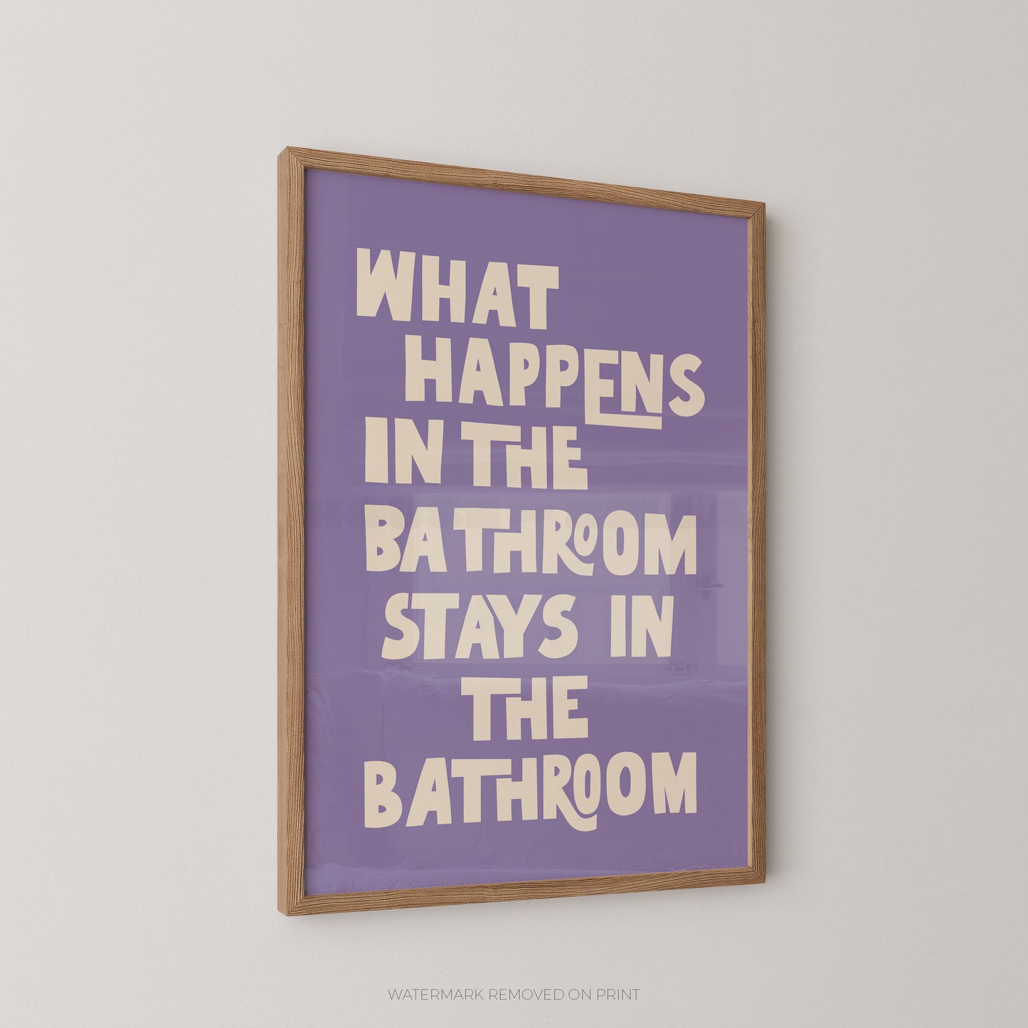 Funny bathroom wall art print in a wood frame – bold lilac and cream chunky typography on a light pink background reading "What Happens In The Bathroom Stays In The Bathroom"