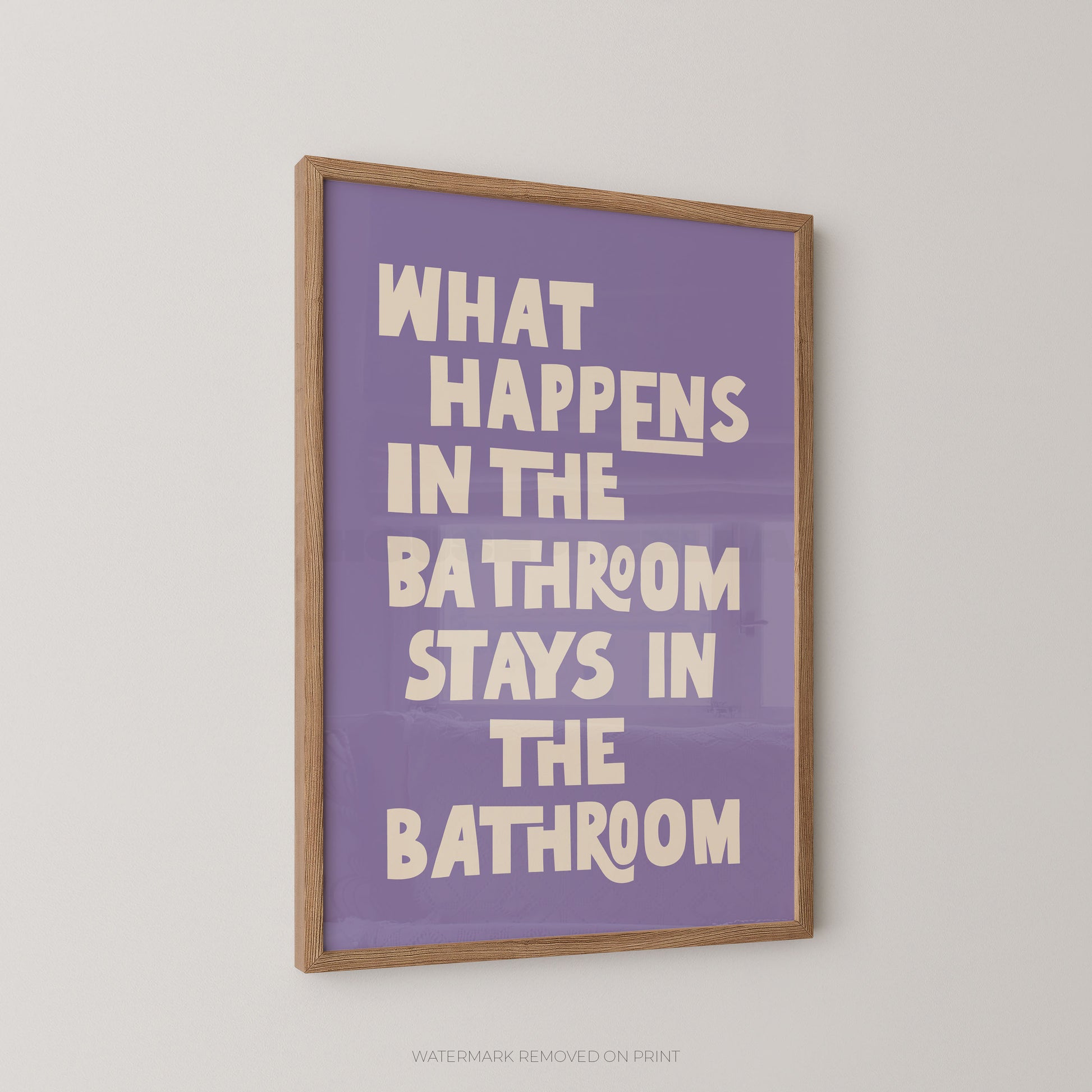 Funny bathroom wall art print in a wood frame – bold lilac and cream chunky typography on a light pink background reading "What Happens In The Bathroom Stays In The Bathroom"