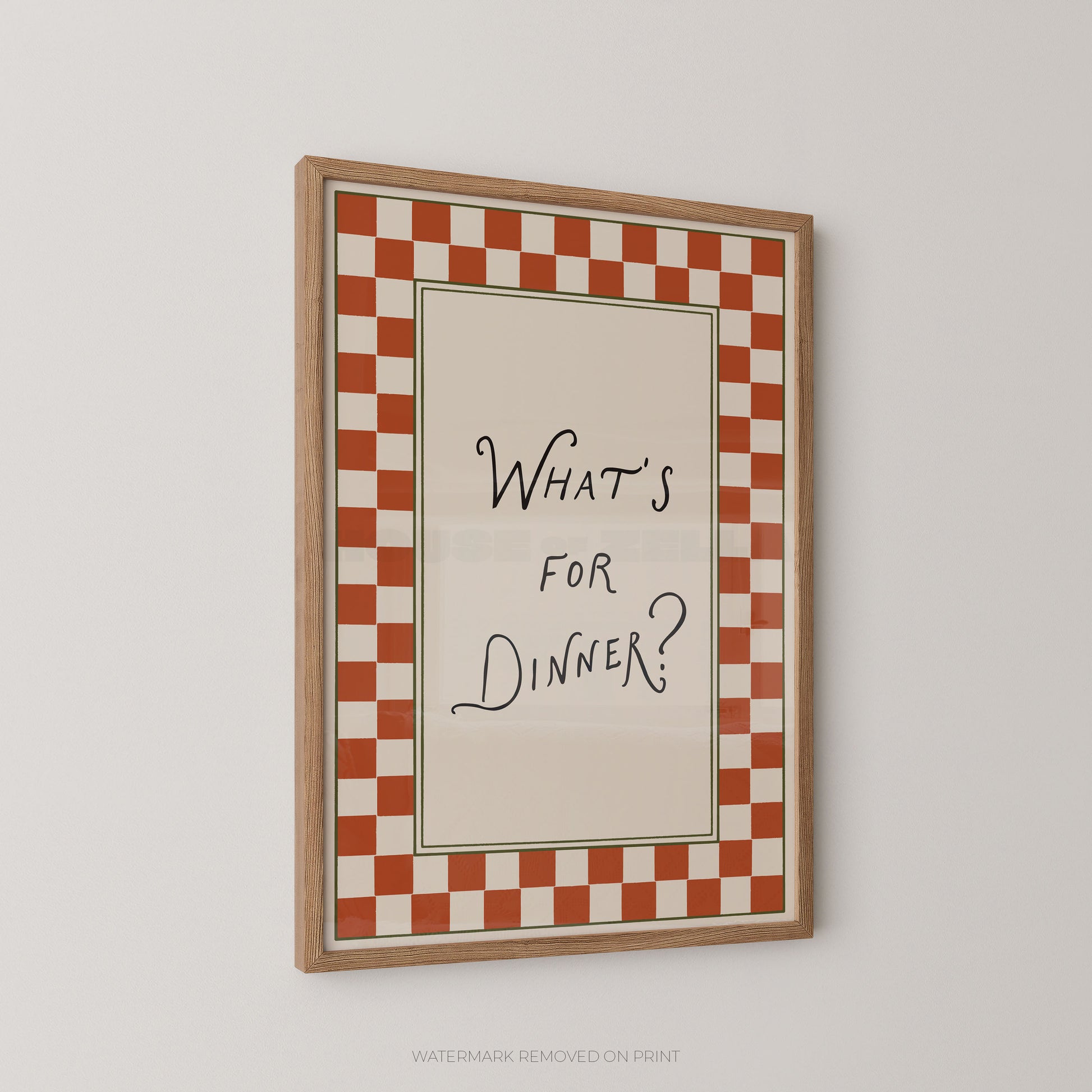 A framed wall art print with a red and white checkered border and the handwritten text 'WHAT'S FOR DINNER?' in black on a cream center panel, shown hanging on a light gray wall.
