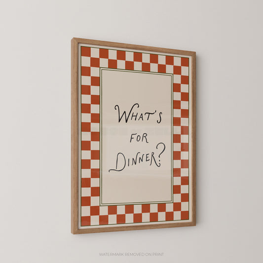 A framed wall art print with a red and white checkered border and the handwritten text 'WHAT'S FOR DINNER?' in black on a cream center panel, shown hanging on a light gray wall.