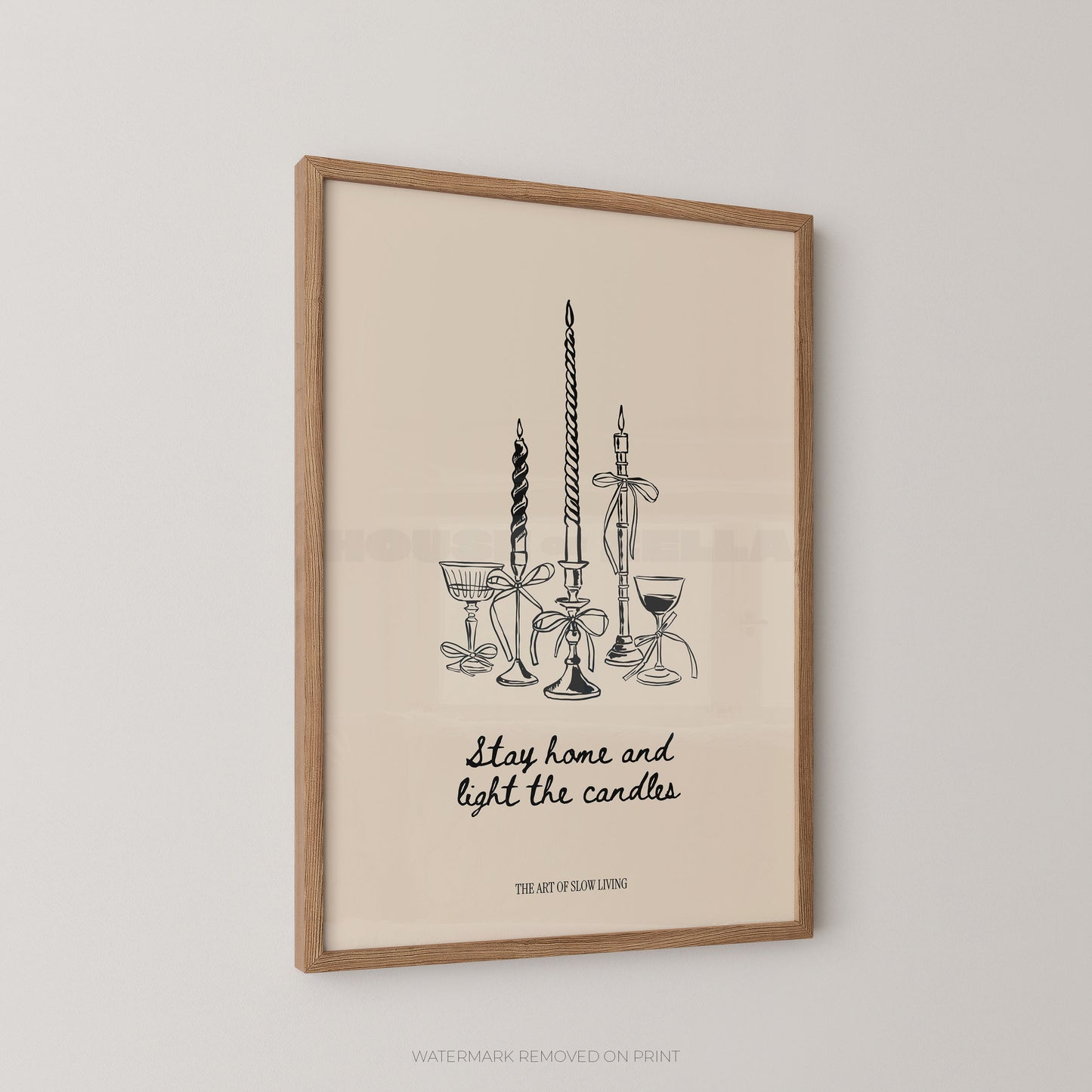Framed wall art print with a minimalist black line drawing of candles, goblets, and a candlestick, plus the phrase 'Stay home and light the candles.' The print has a warm cream background and is shown in a light wood frame against a light gray wall.