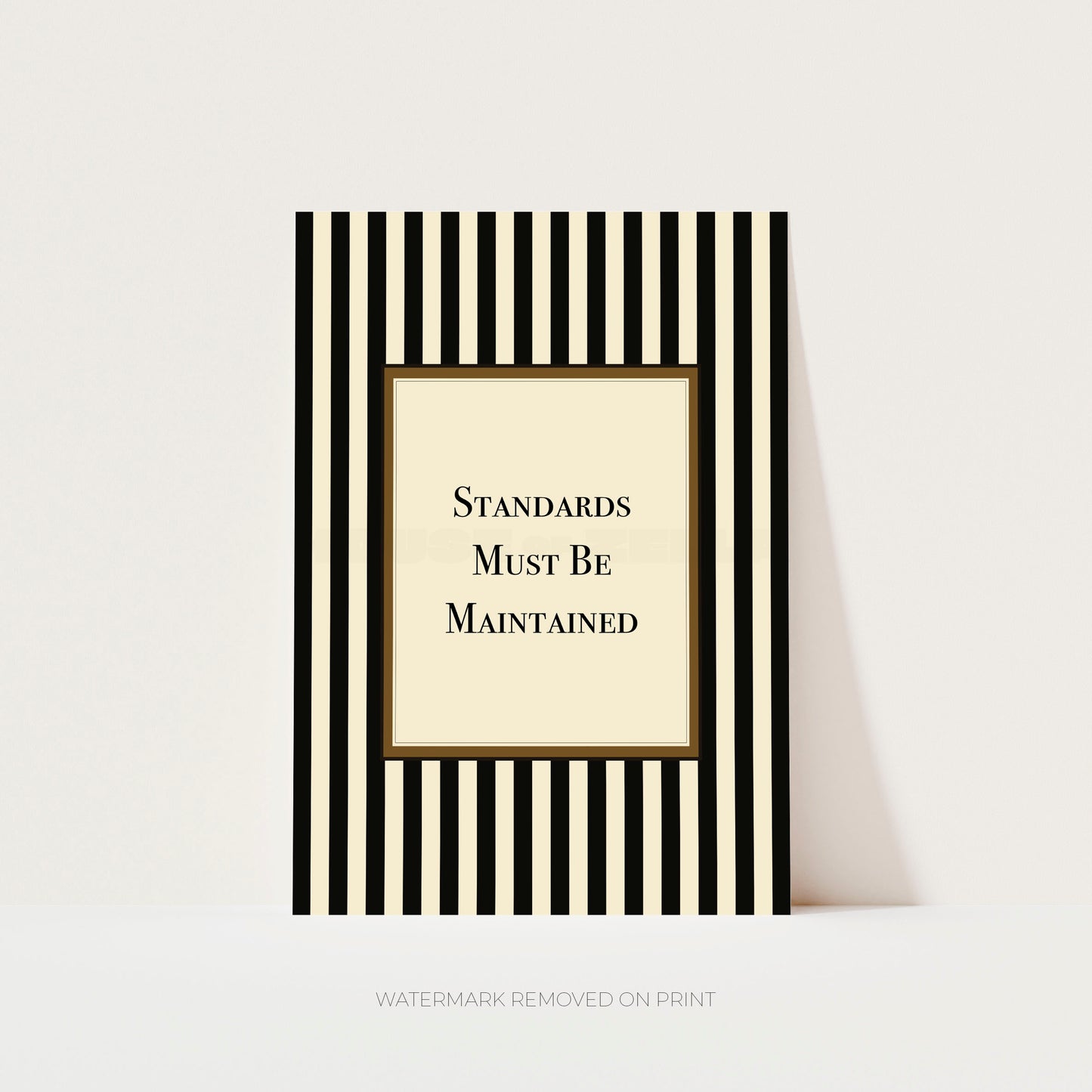 A vertical art print with black and cream stripes and a central cream panel reading 'STANDARDS MUST BE MAINTAINED' in black serif text, shown against a light neutral background.