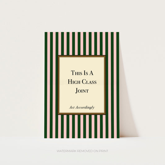 A rectangular printed card or poster with vertical dark green and pale pink stripes, featuring a cream center panel with the text 'This Is A High Class Joint' and smaller script text 'Act Accordingly.' The item is photographed against a light neutral background with a soft shadow to the right.