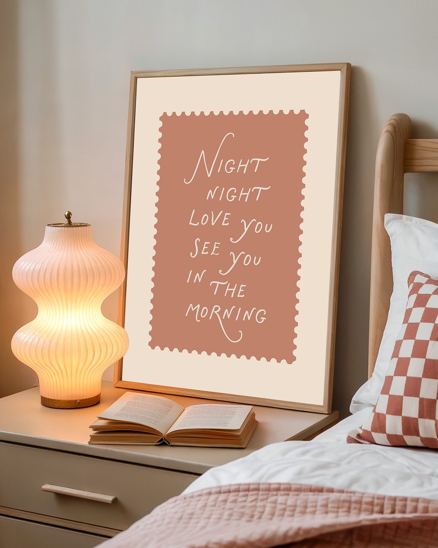 Framed print with 'Night night love you see you in the morning' text on a bedside table with a lamp and open book.
