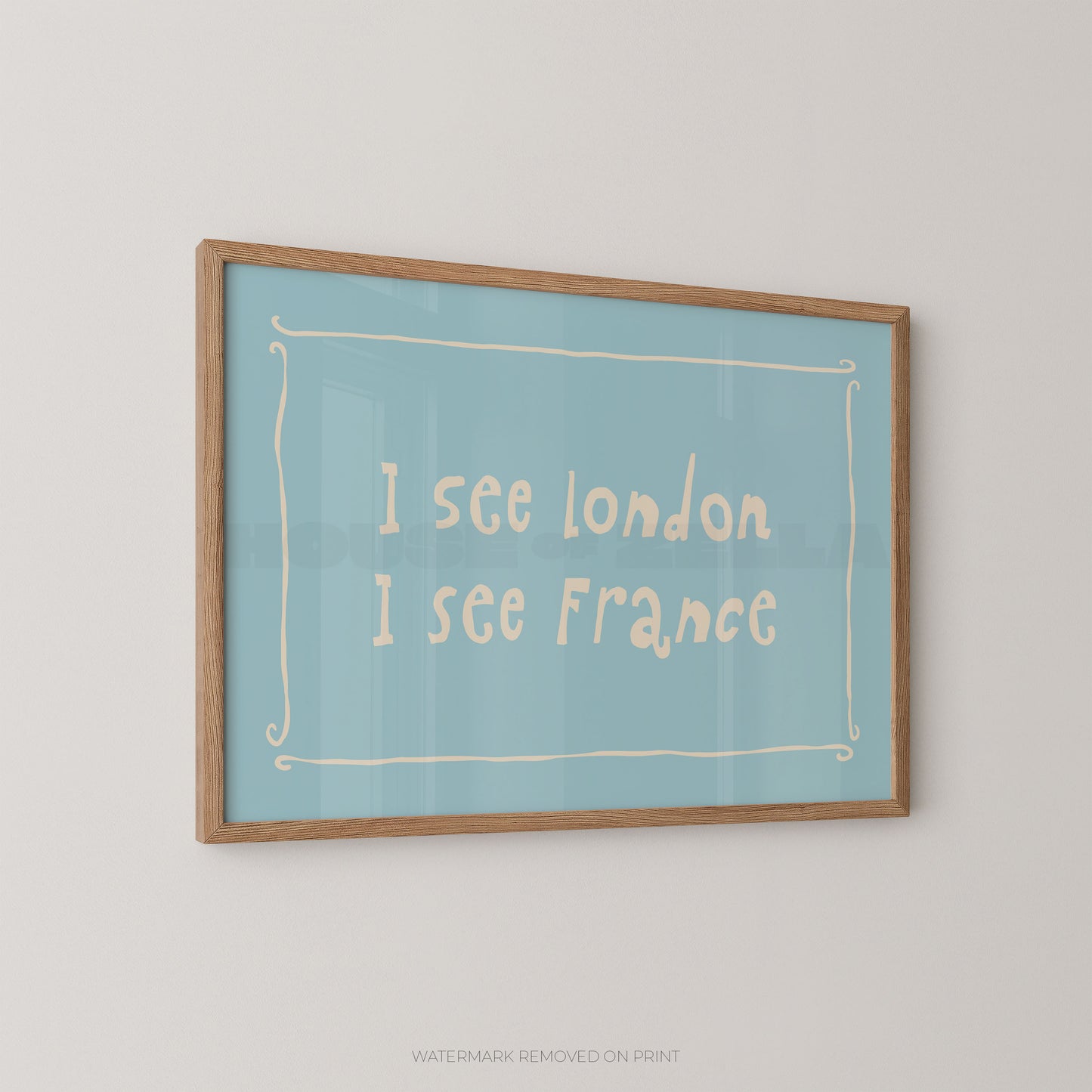 A framed typographic wall art print hanging on a light gray wall. The print has a pale blue background with cream handwritten text reading 'I see london I see France' inside a thin cream decorative border, and a natural wood frame.