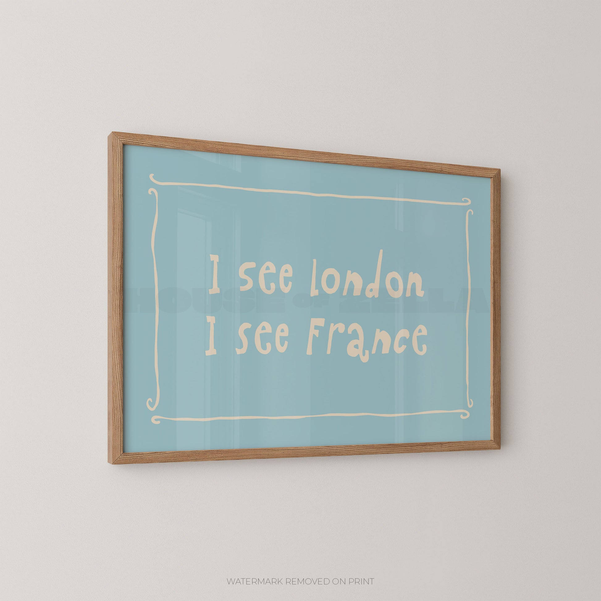 A framed typographic wall art print hanging on a light gray wall. The print has a pale blue background with cream handwritten text reading 'I see london I see France' inside a thin cream decorative border, and a natural wood frame.