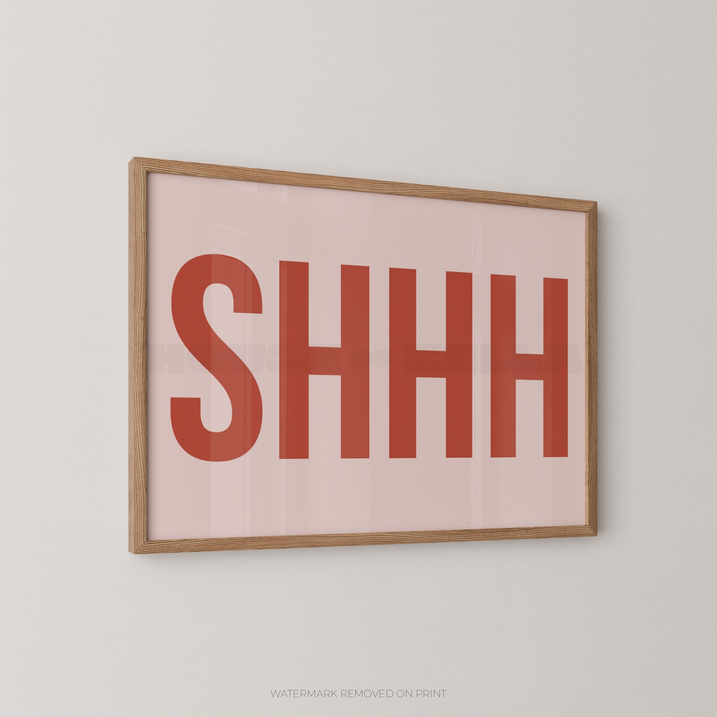 Framed typographic wall art with the word 'SHHH' in large muted red letters on a pale pink background, shown hanging on a light gray wall.