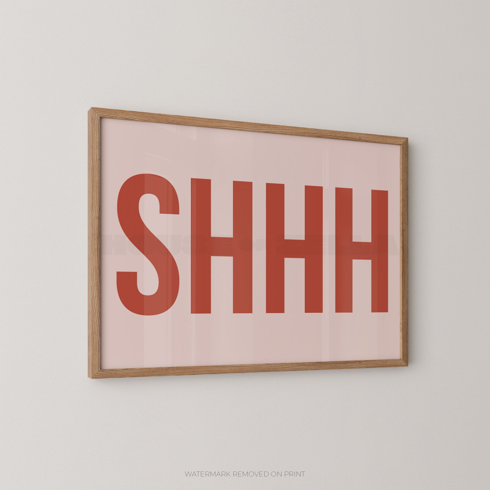 Framed typographic wall art with the word 'SHHH' in large muted red letters on a pale pink background, shown hanging on a light gray wall.