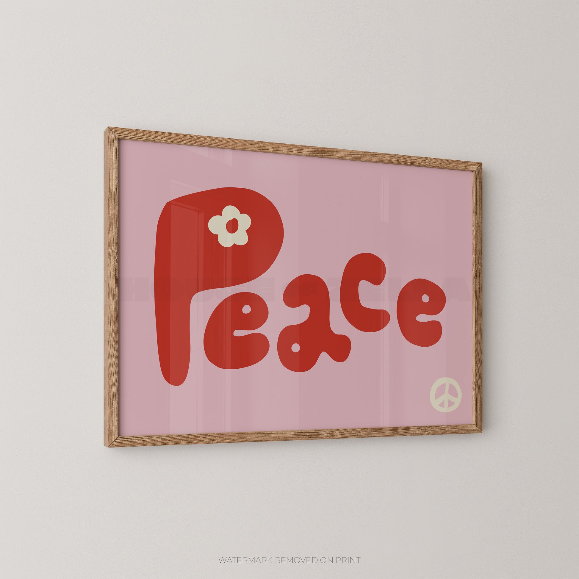 A framed retro-style art print featuring the word 'Peace' in red retro lettering on a pink background, with a small white flower on the letter 'P' and a peace sign in the lower right. The print is housed in a light natural wood frame and is mounted on a plain light gray wall.