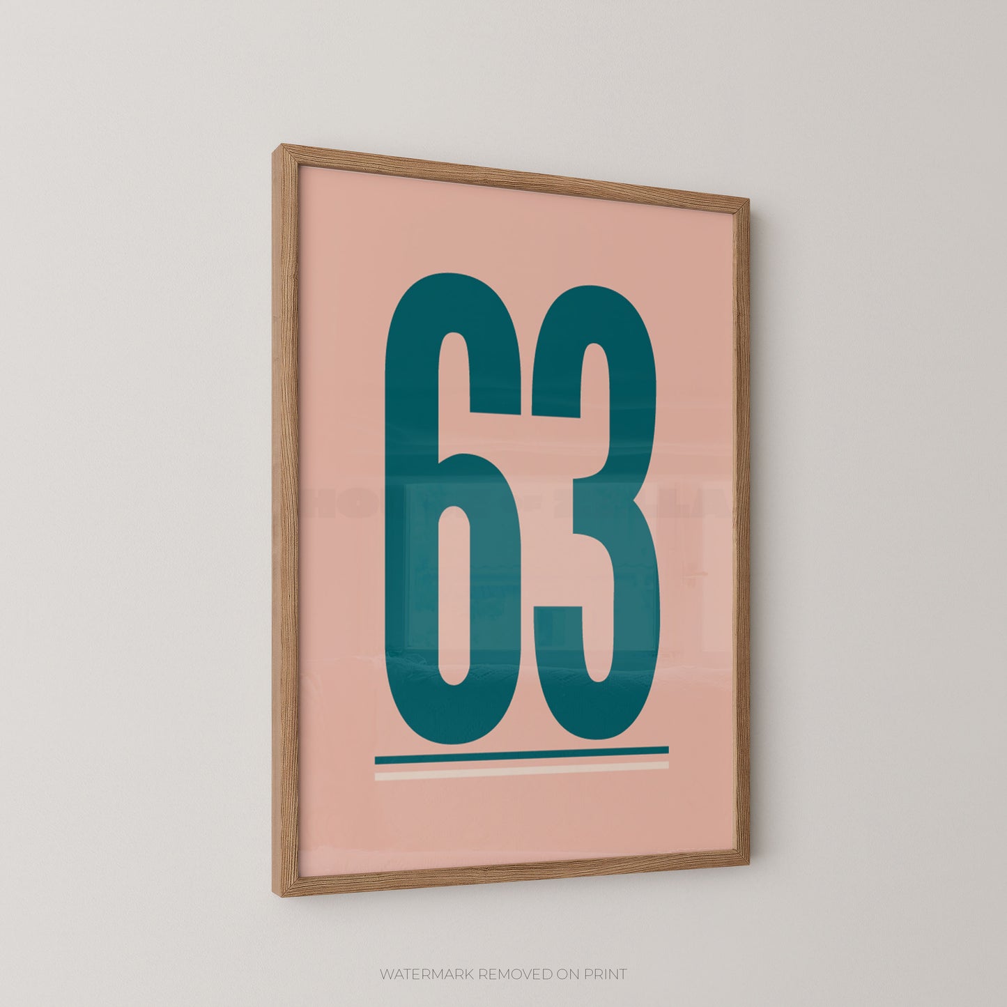 Framed minimalist wall art featuring the number 63 in teal on a blush pink background, hung on a light gray wall.
