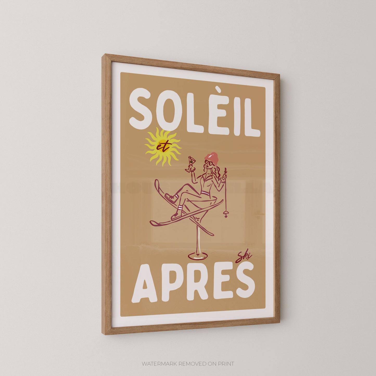 A framed vintage-style poster with the French text “SOLÉIL et APRES” in large white letters on a tan background, featuring a simple line drawing of a skier and a yellow sun. The print is mounted in a light wood frame and shown hanging on a light gray wall.