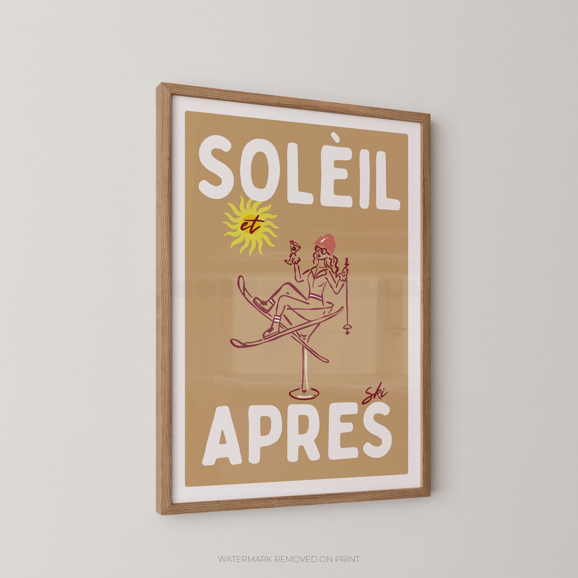 A framed vintage-style poster with the French text “SOLÉIL et APRES” in large white letters on a tan background, featuring a simple line drawing of a skier and a yellow sun. The print is mounted in a light wood frame and shown hanging on a light gray wall.