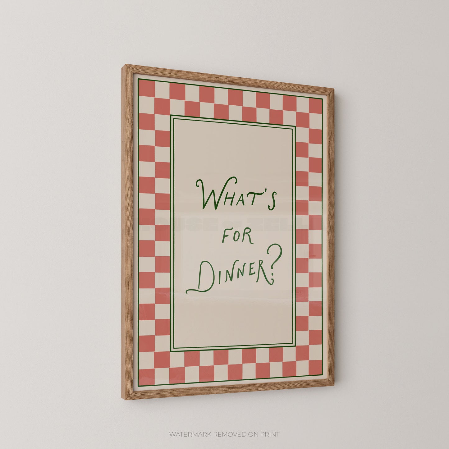 A framed typographic wall art print with a red and white checkered border and the handwritten text “WHAT’S FOR DINNER?” in green inside a light wood frame, shown hanging on a plain light gray wall.