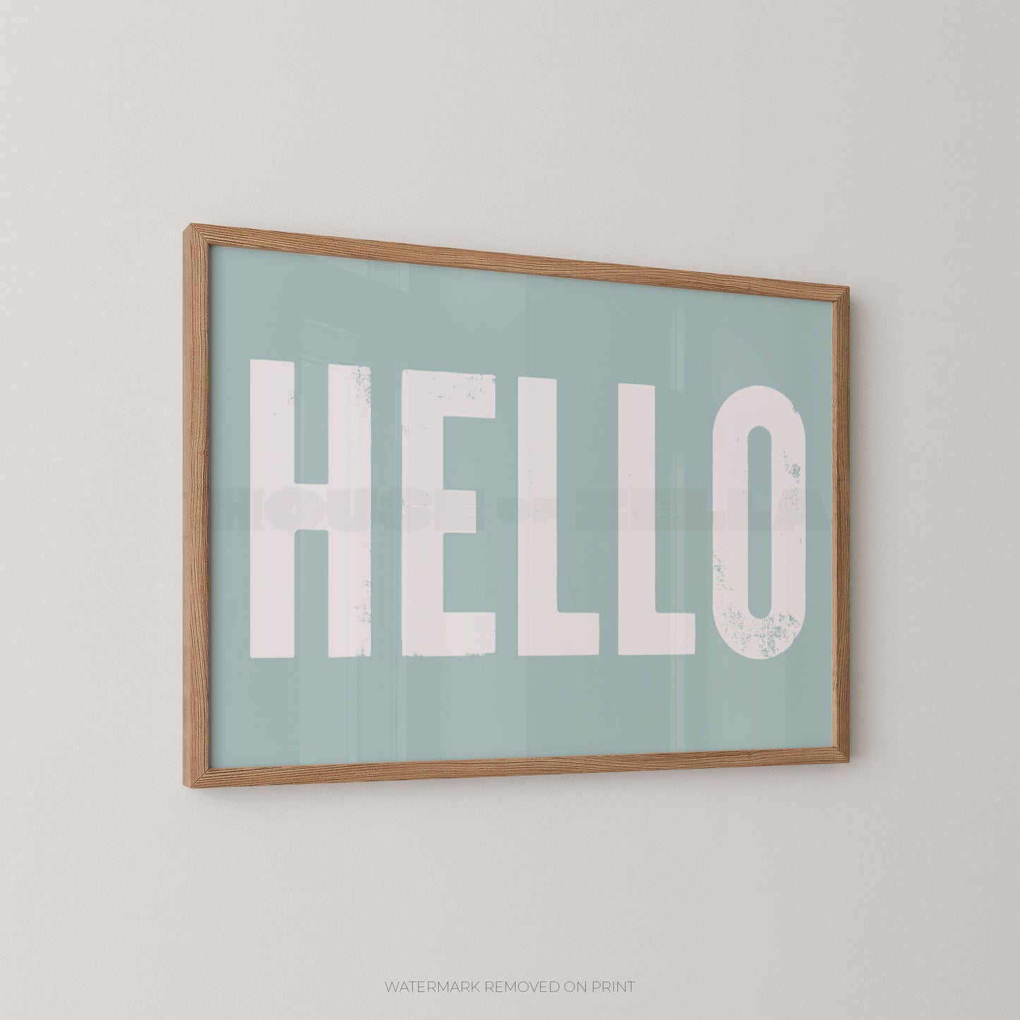 Framed wall art print with the word "HELLO" in large distressed white letters on a pale blue background, shown hanging on a light neutral wall.