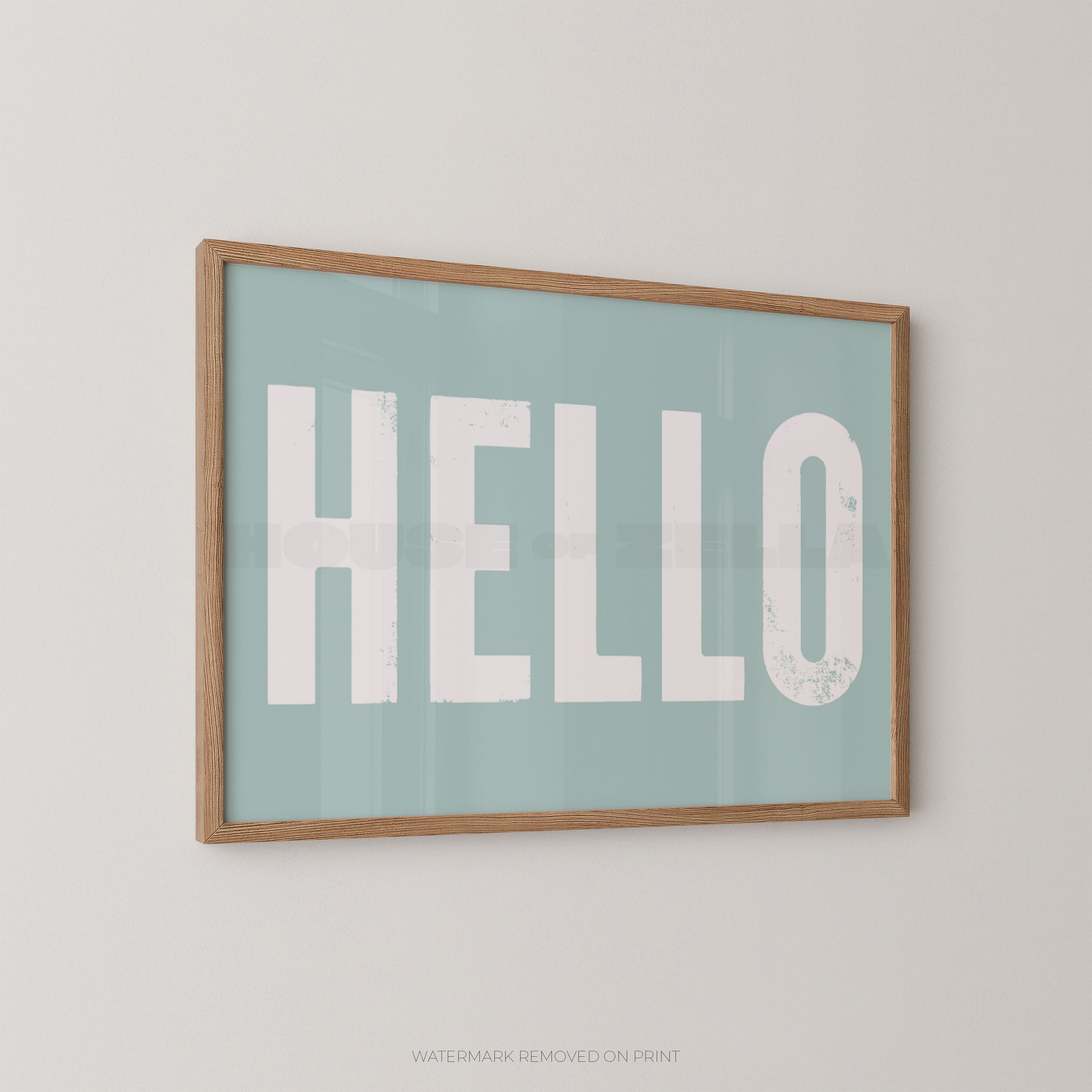 Framed wall art print with the word "HELLO" in large distressed white letters on a pale blue background, shown hanging on a light neutral wall.