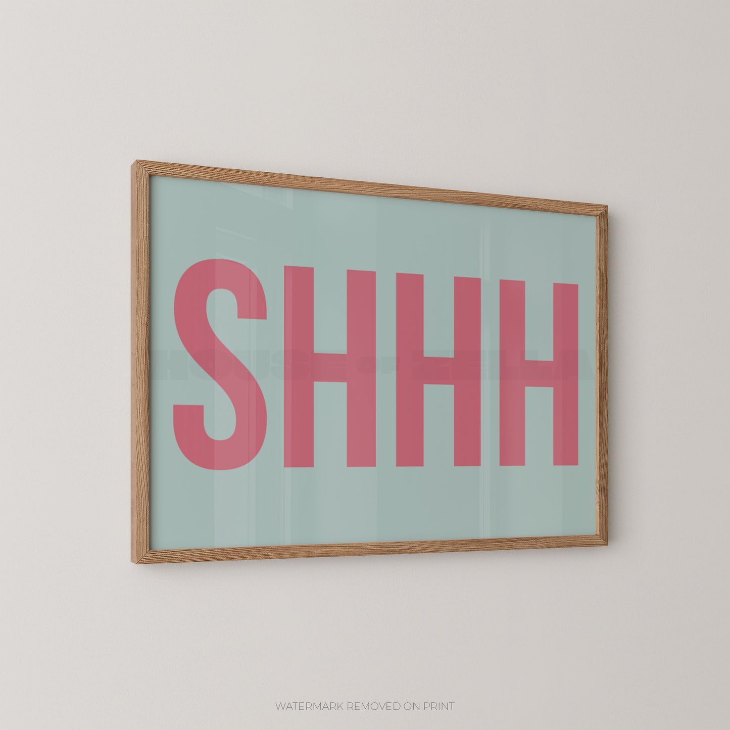 Framed typographic wall art with the word “SHHH” in large pink letters on a pale mint background, shown hanging on a light neutral wall.