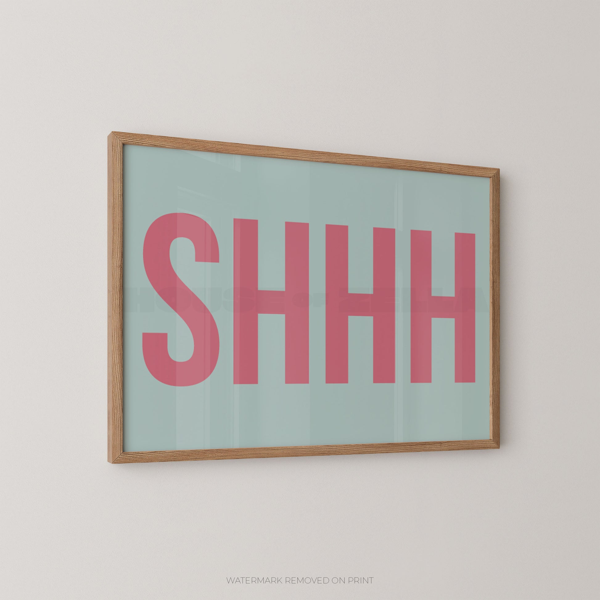 Framed typographic wall art with the word “SHHH” in large pink letters on a pale mint background, shown hanging on a light neutral wall.