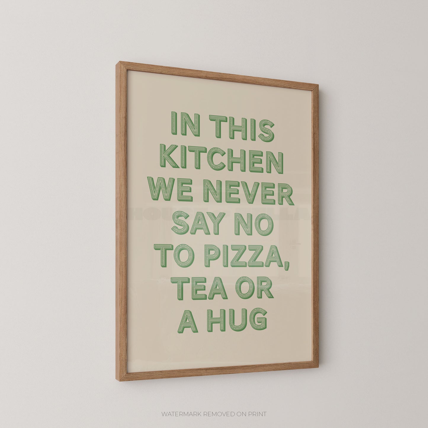A framed typographic wall art print with the phrase “IN THIS KITCHEN WE NEVER SAY NO TO PIZZA, TEA OR A HUG” in green letters on a warm cream background, shown hanging on a light gray wall.