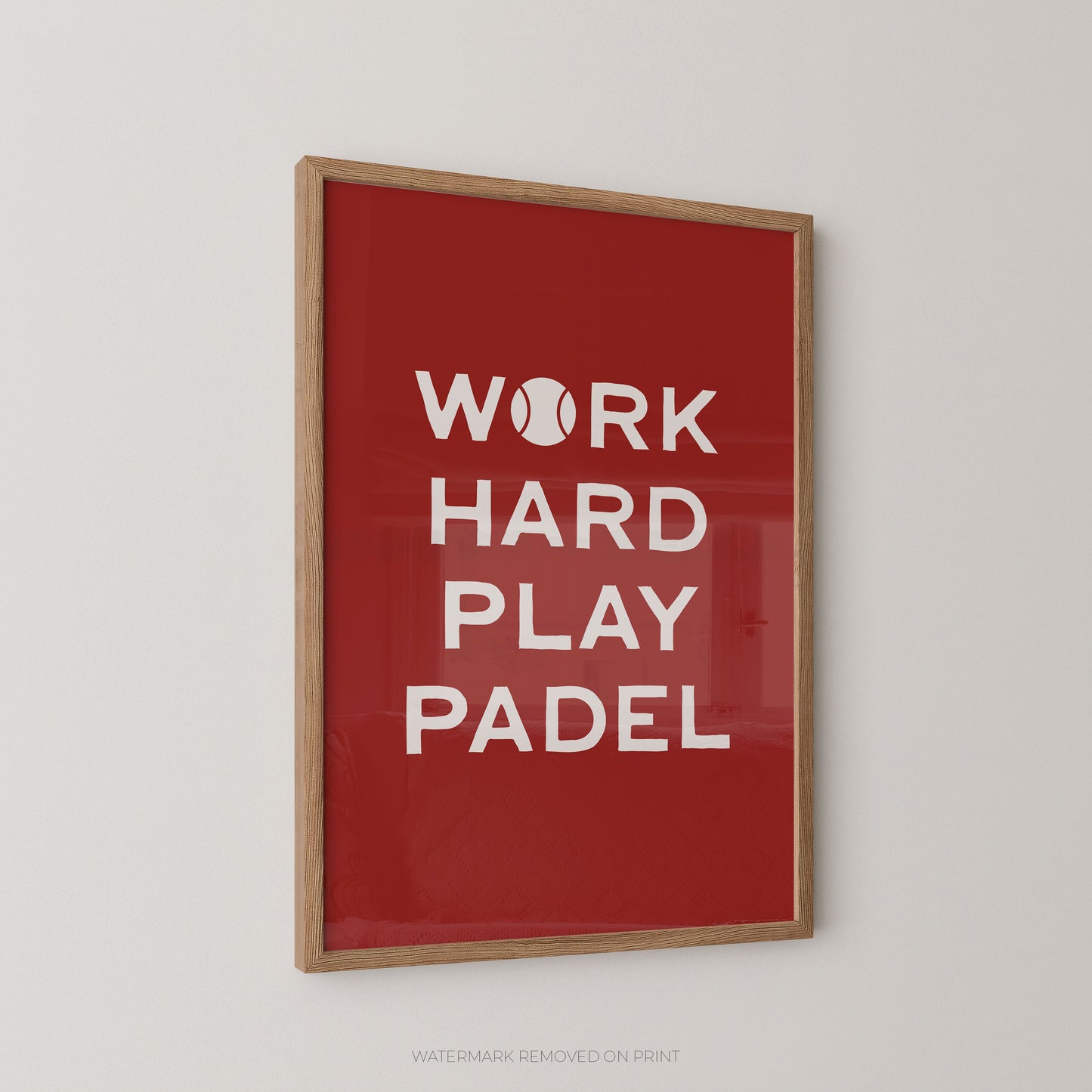 Framed wall art print with the phrase 'WORK HARD PLAY PADEL' in white text on a red background, shown hanging on a light gray wall.