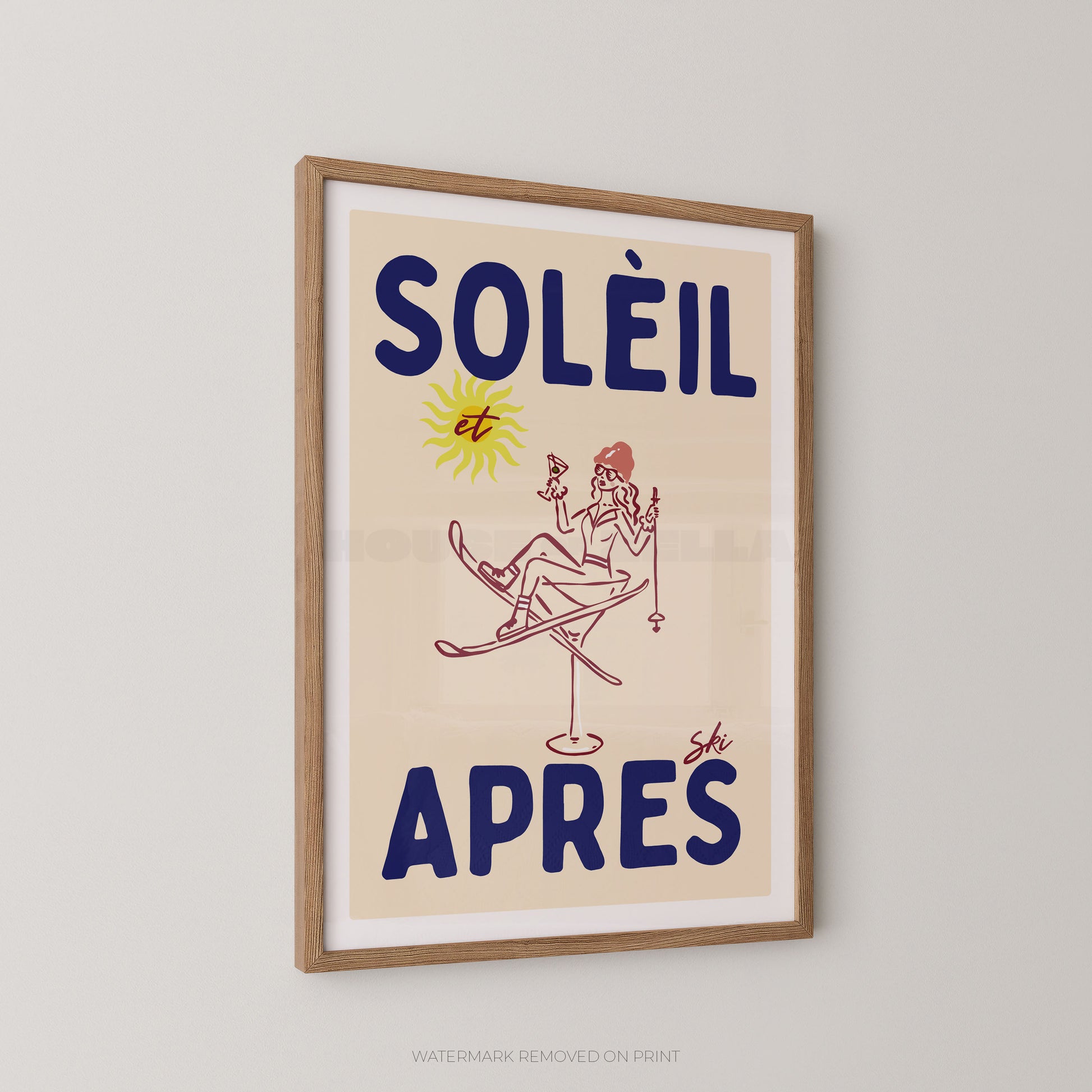 A framed vintage-style poster with the French text “SOLÉIL et APRÈS” in dark blue, featuring a simple illustration of a woman skiing with a yellow sun graphic, hanging on a light gray wall.