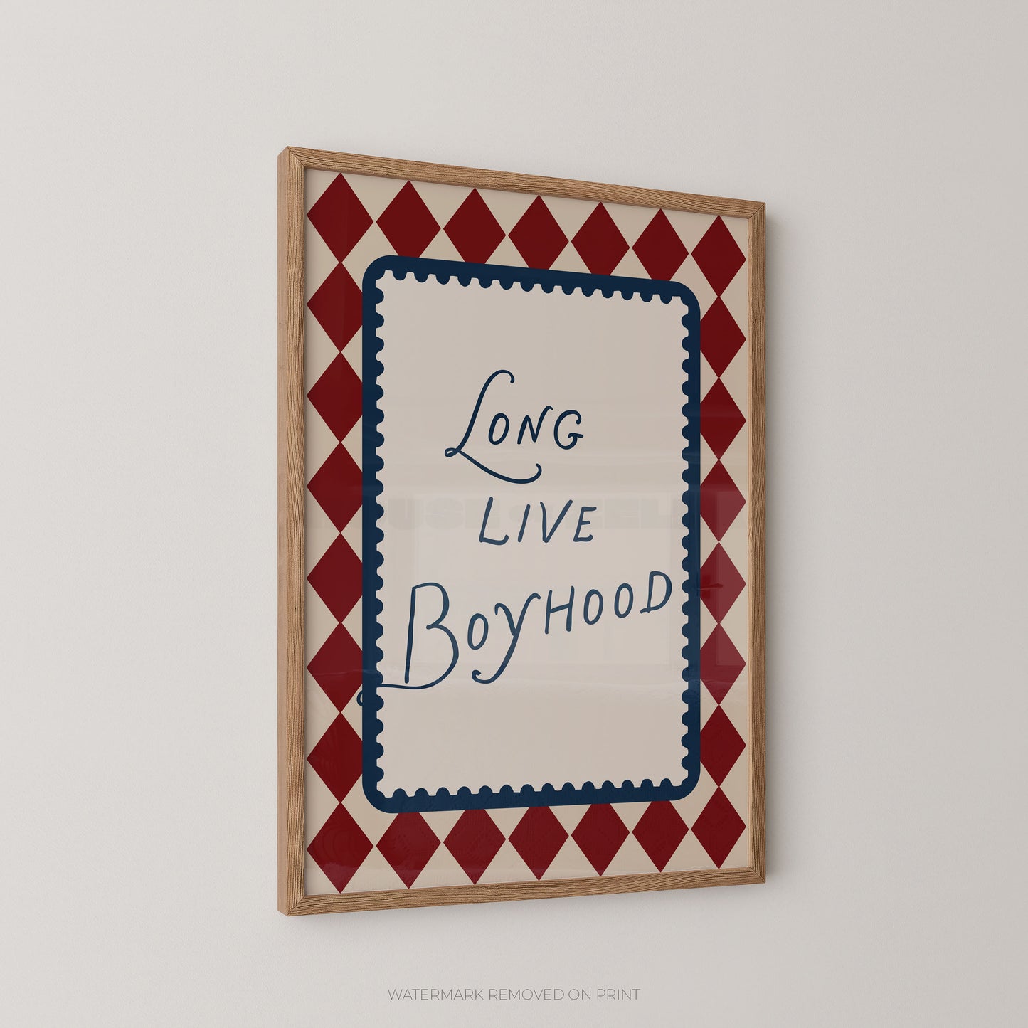 Framed wall art print with the phrase 'Long Live Boyhood' in blue script inside a cream center panel, surrounded by a red and cream diamond border, shown hanging on a light gray wall.