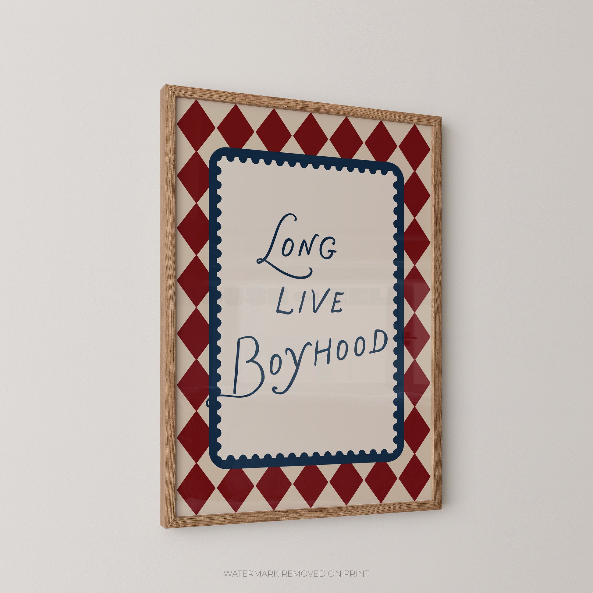 Framed wall art print with the phrase 'Long Live Boyhood' in blue script inside a cream center panel, surrounded by a red and cream diamond border, shown hanging on a light gray wall.