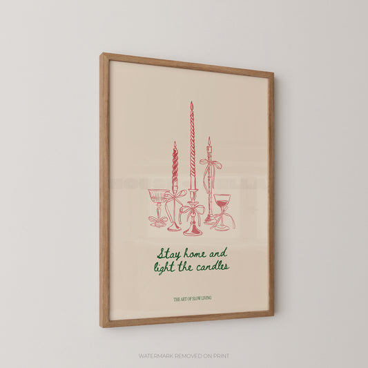Framed art print featuring red line drawings of candles and glassware with the phrase 'Stay home and light the candles' in green script, hanging on a light gray wall.