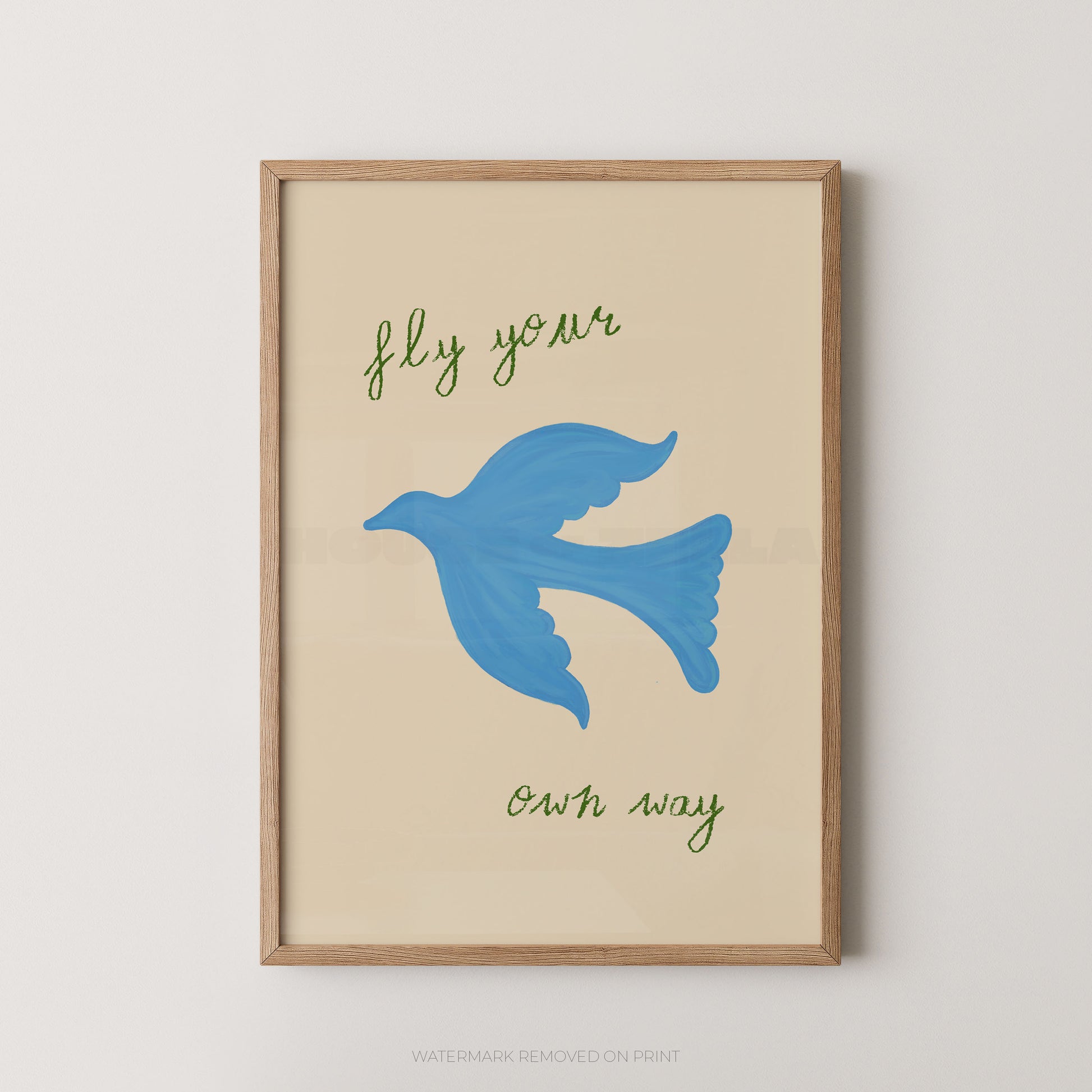 Framed wall art print with a light wood frame, featuring a blue bird illustration and the phrase 'fly your own way' in green script on a warm cream background.