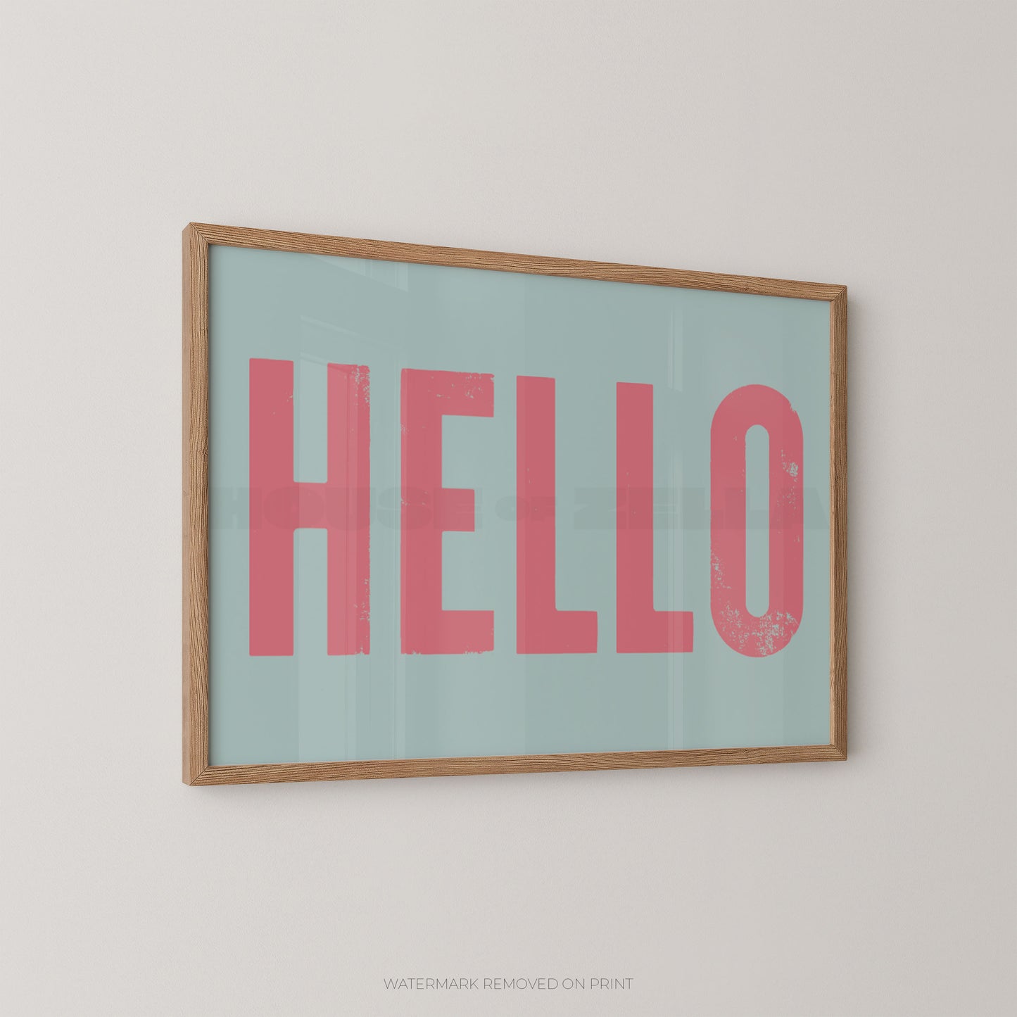 Framed typographic wall art hanging on a light wall, featuring the word "HELLO" in large pink letters on a pale blue background with a natural wood frame.