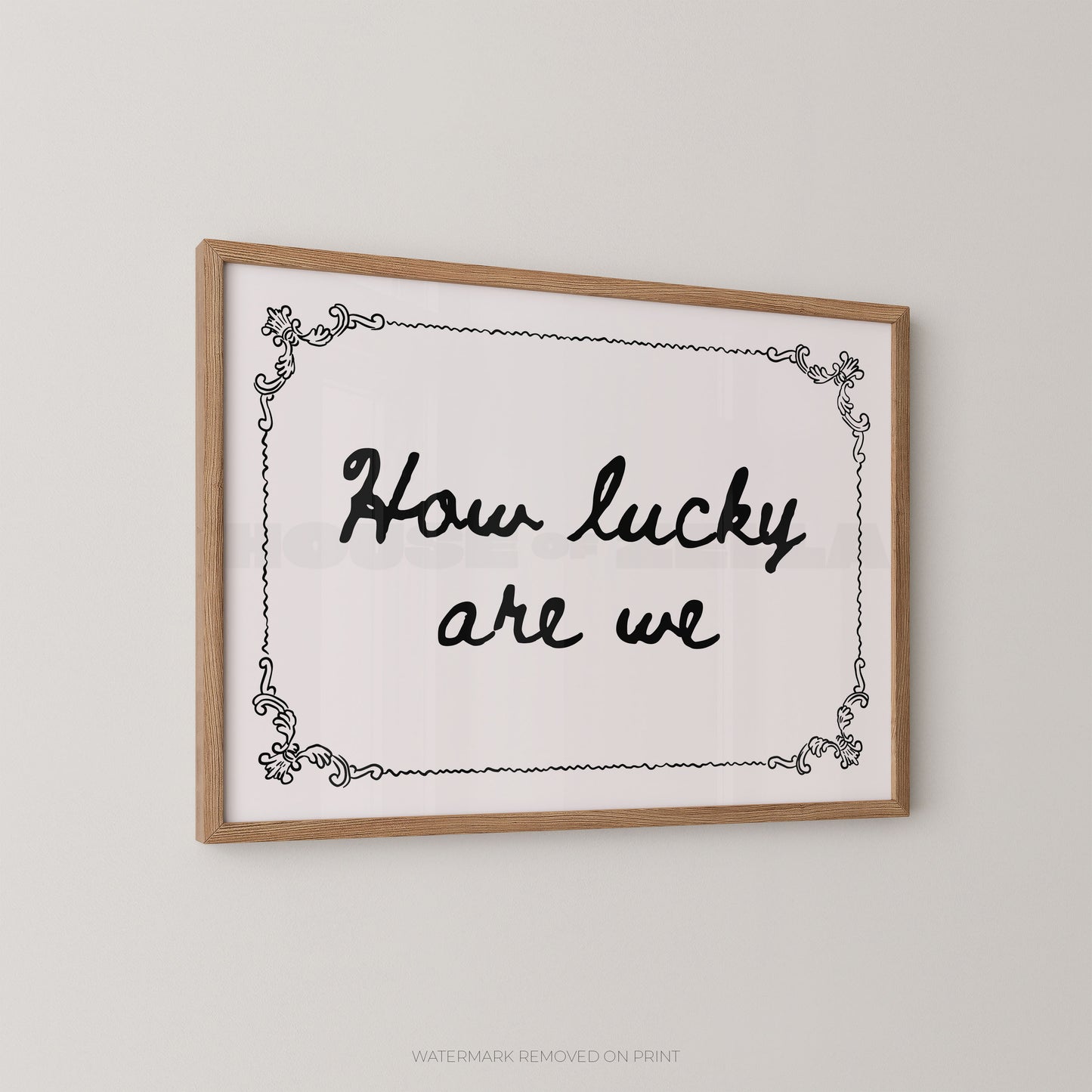 Framed wall art print with the phrase “How lucky are we” in black script inside a light wood frame, shown hanging on a plain light gray wall.