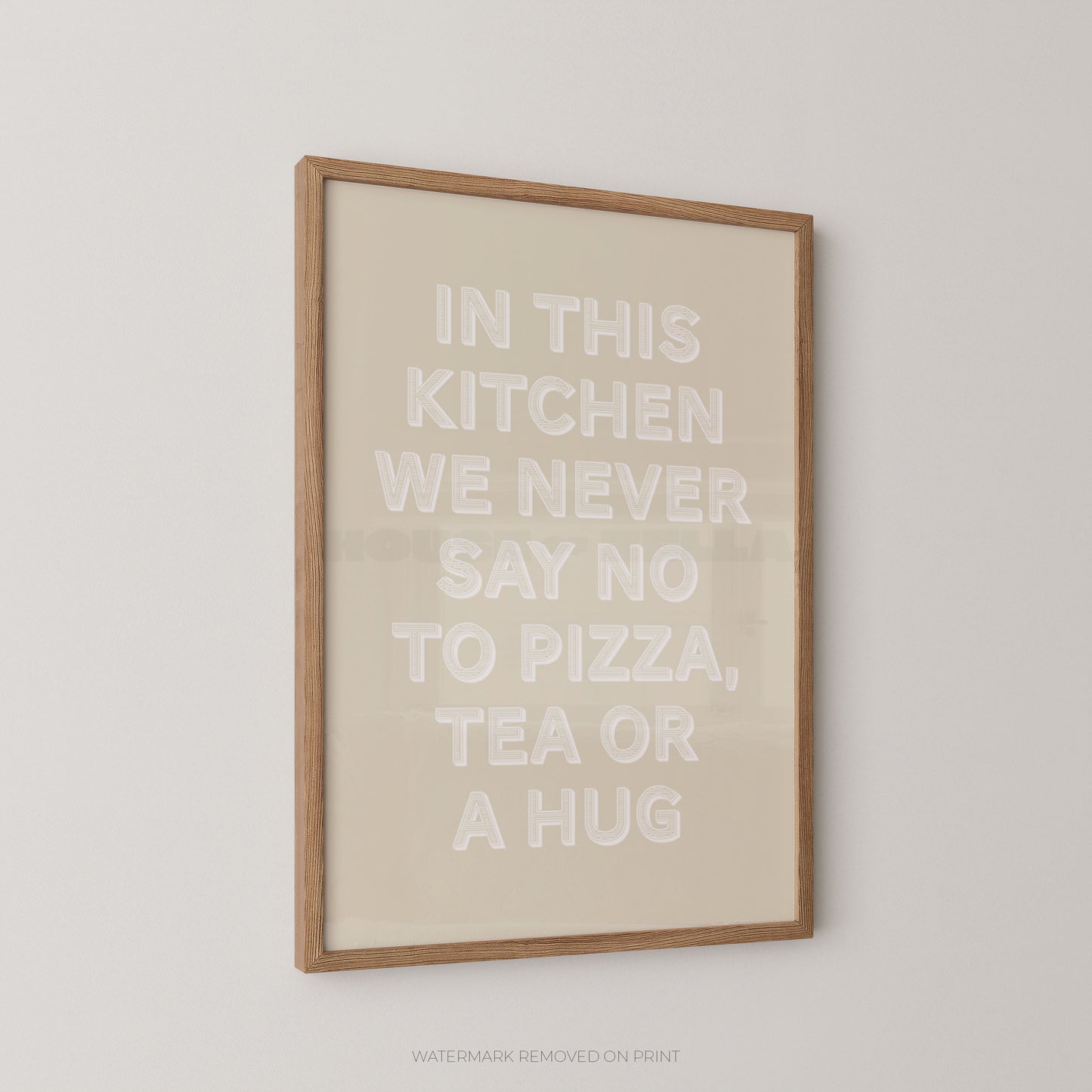 A framed typographic wall art print with the phrase “IN THIS KITCHEN WE NEVER SAY NO TO PIZZA, TEA OR A HUG” in raised white lettering on a warm cream background, shown hanging on a light neutral wall.