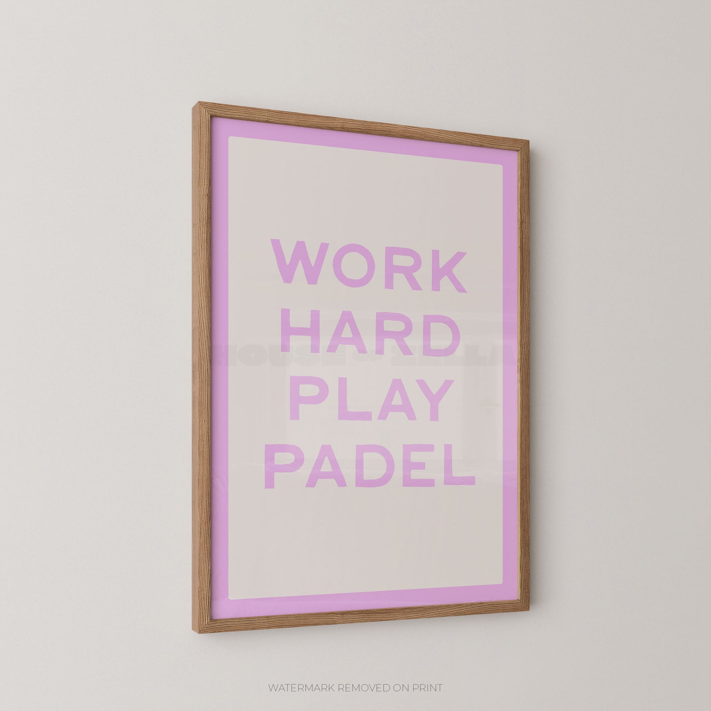 A framed typographic wall art print with the words “WORK HARD PLAY PADEL” in lavender-purple lettering on a white background with a lavender border, set in a light natural wood frame against a light gray wall.