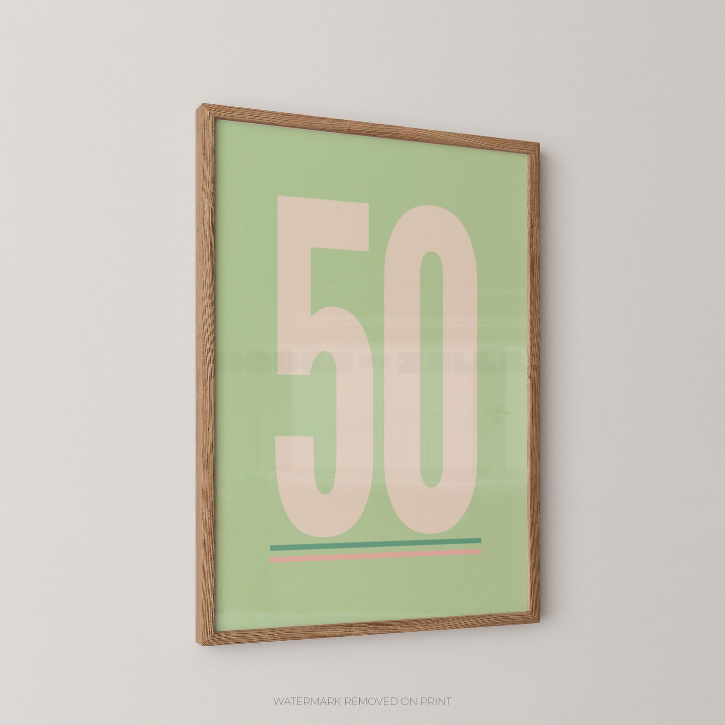 A framed minimalist art print featuring the number '50' in a pale pink color on a light sage green background, enclosed in a natural wood frame and displayed on a light gray wall.
