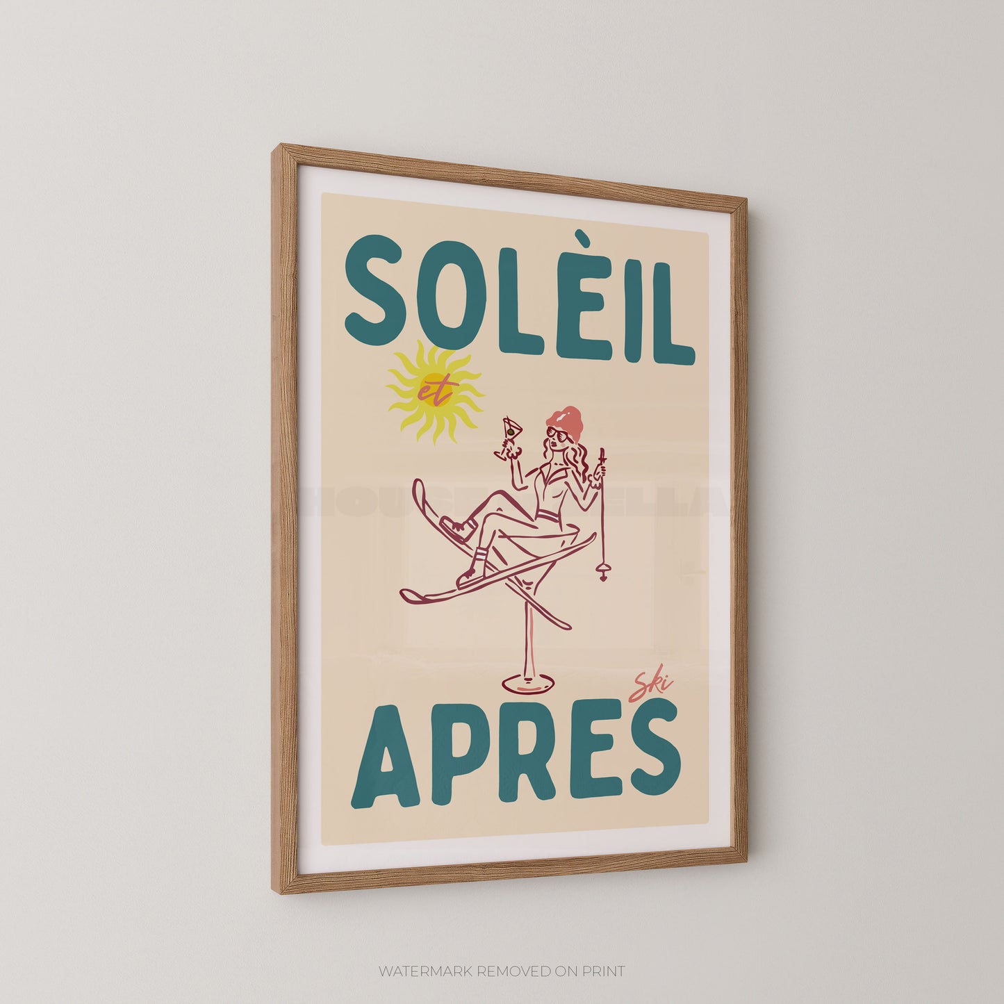 A framed vintage-style poster with the French text “SOLÉIL APRES” in teal, featuring a simple illustration of a woman skiing under a yellow sun on a cream background, shown hanging on a light gray wall.
