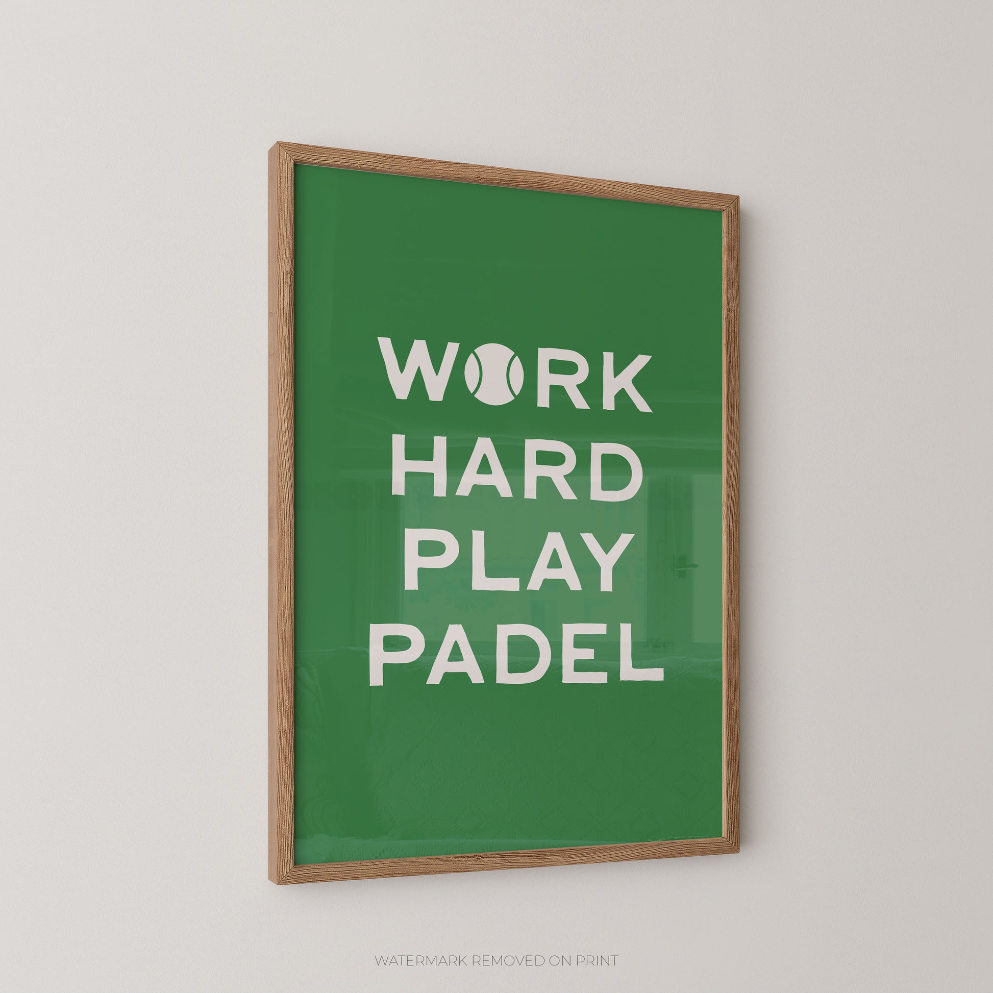 A framed wall art print with a green background and white text reading “WORK HARD PLAY PADEL,” with a tennis ball icon replacing the letter O in “WORK.” The print is shown hanging on a light gray wall.