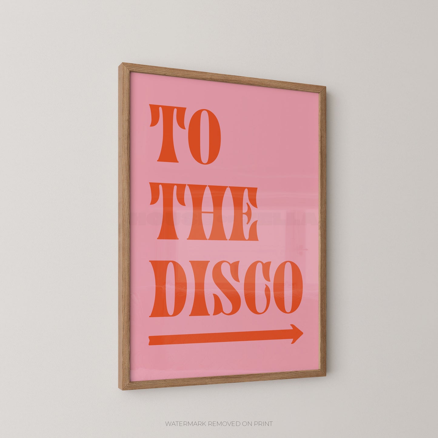 A framed typographic wall art print with the words “TO THE DISCO” in orange on a pink background, shown hanging on a light gray wall.