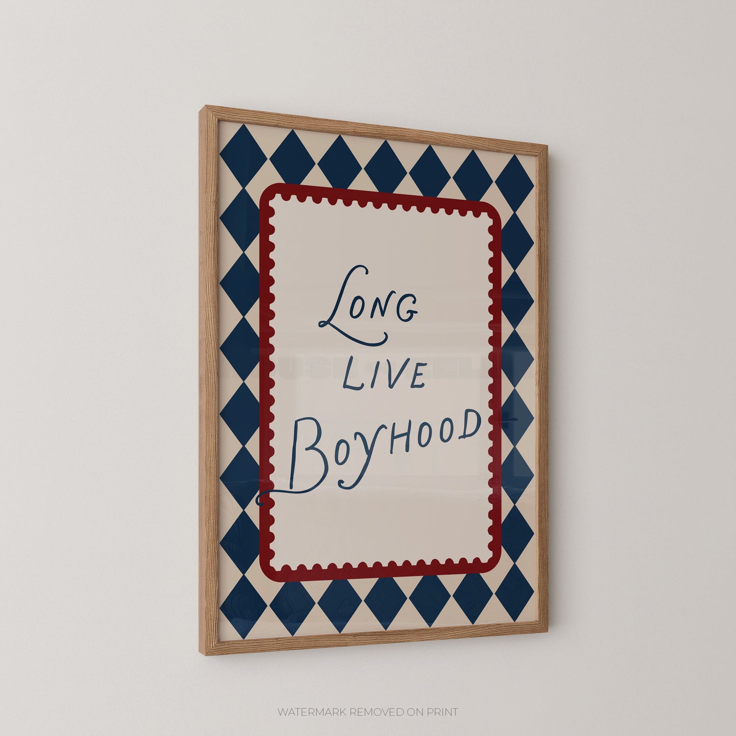 Framed wall art print with the phrase 'Long Live Boyhood' in blue script inside a red scalloped border, surrounded by a navy and cream harlequin diamond pattern, shown hanging on a light gray wall.