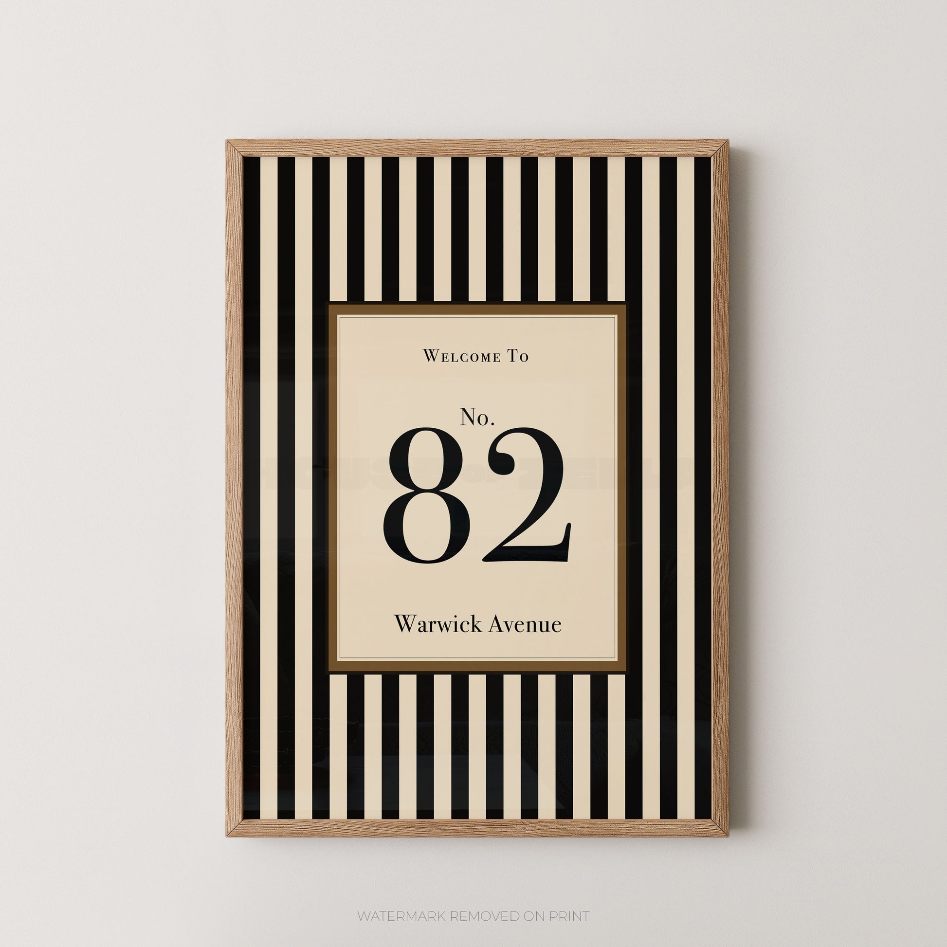 Framed vertical black and cream striped wall art with a central cream panel reading 'Welcome To No. 82 Warwick Avenue', shown hanging on a light neutral wall.