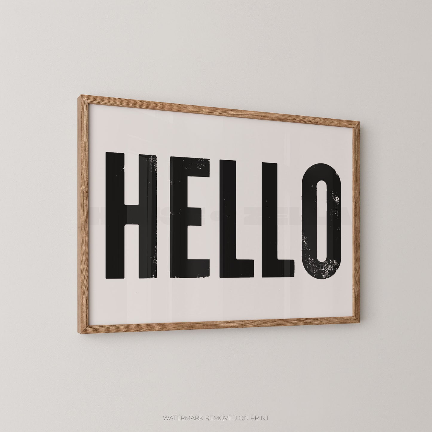 Framed wall art print with the word “HELLO” in large black block letters on a white background, shown hanging on a light gray wall.